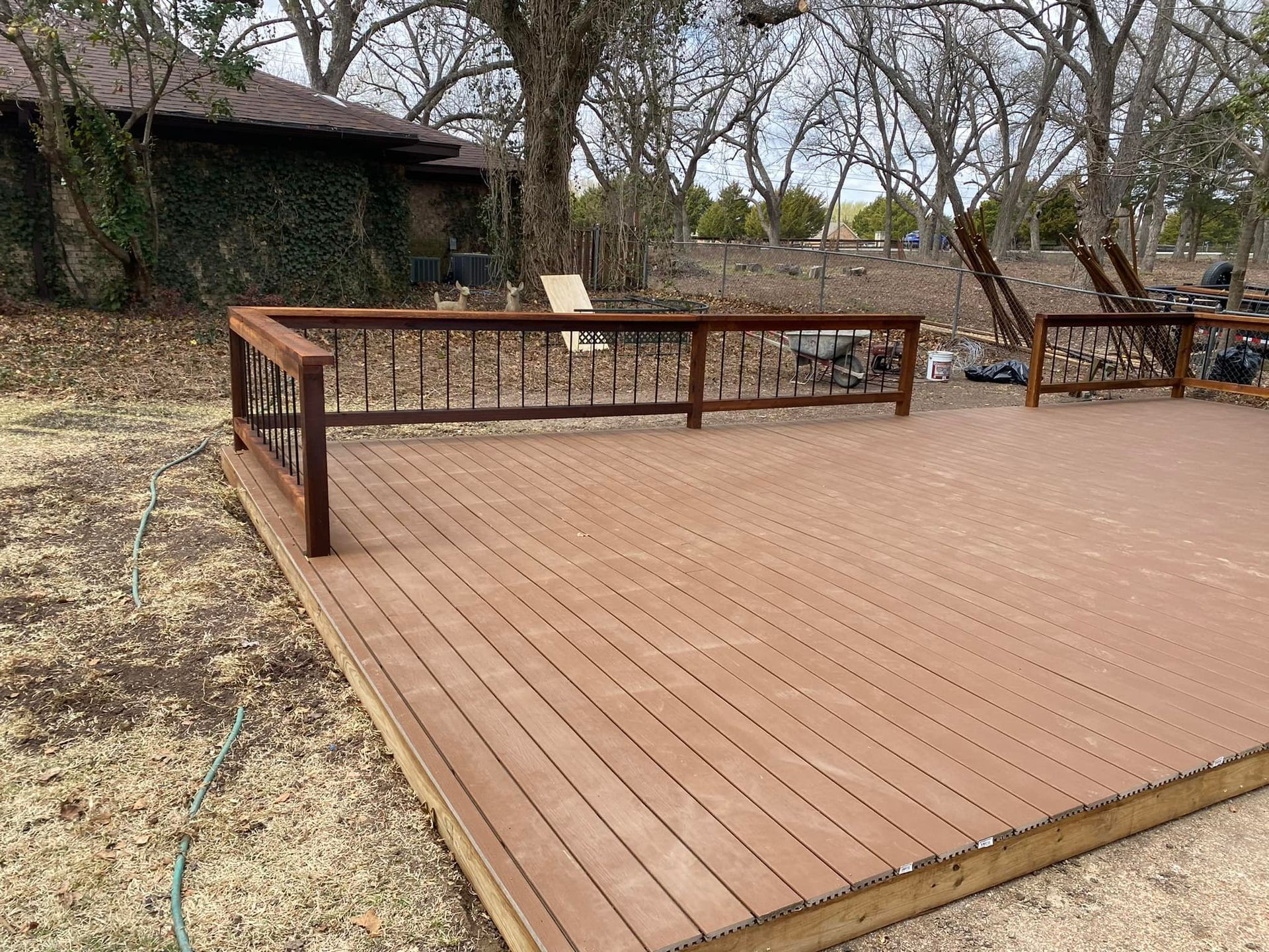 Wooden deck with railing beside a yard and trees, outdoors on a clear day