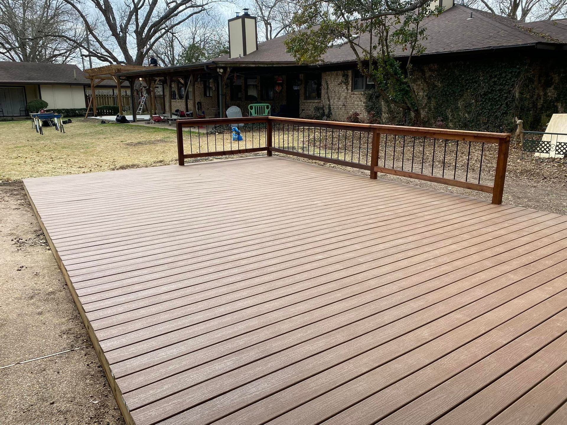 Raised wooden deck in a backyard beside a house, with a metal railing and a grassy yard.