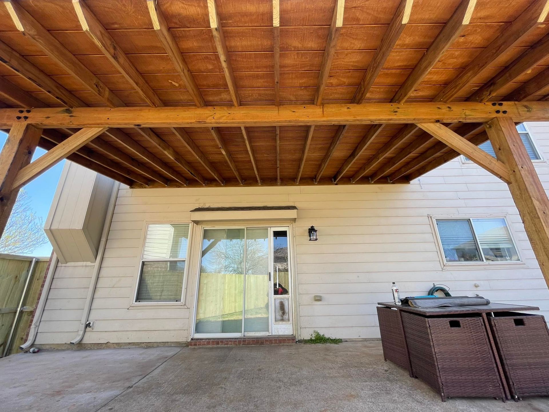 Covered patio with wooden beams, sliding glass door, white siding, and an outdoor storage box.
