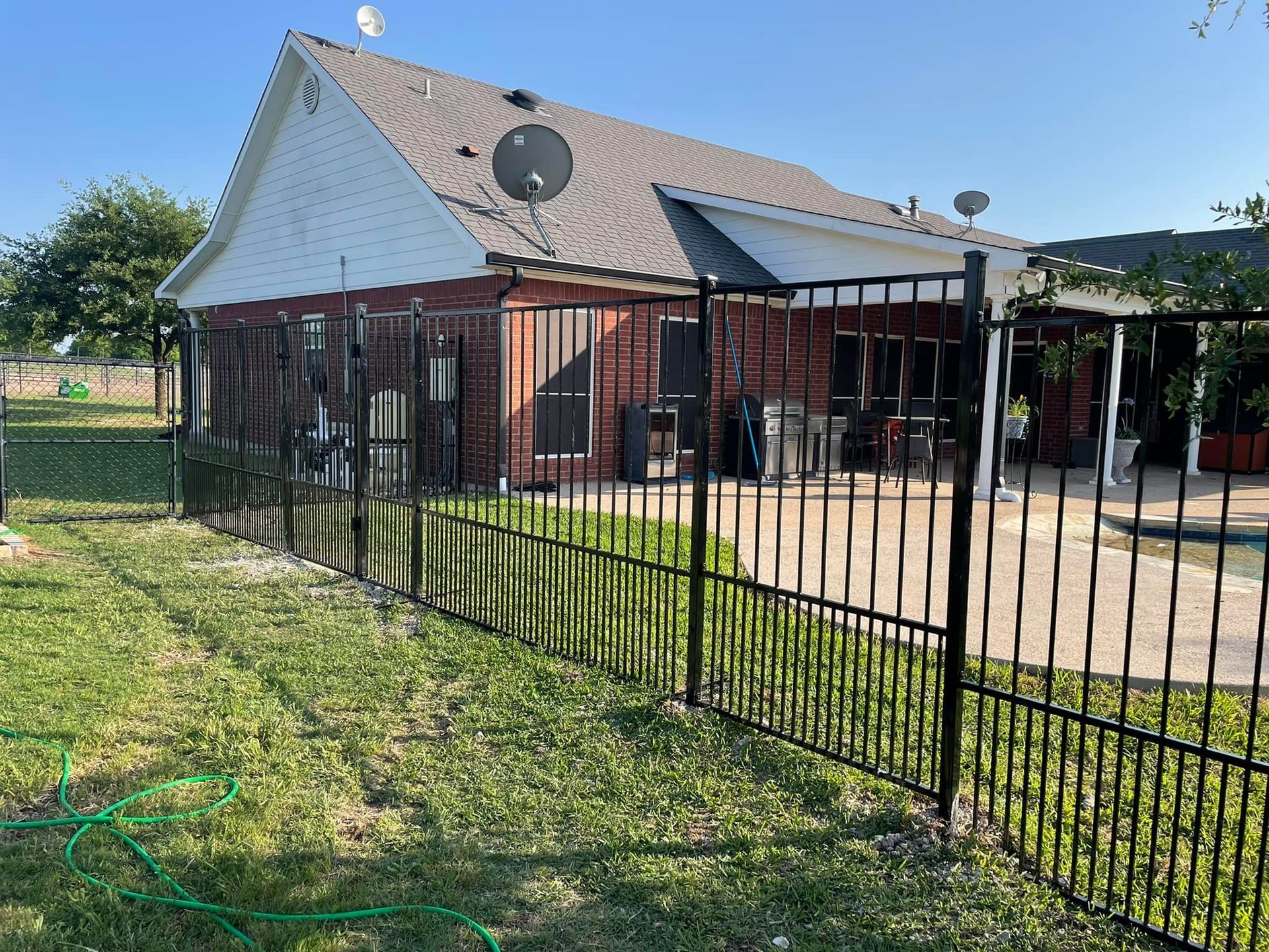 Brick house with a red roof, black fence, and a patio under a clear blue sky.