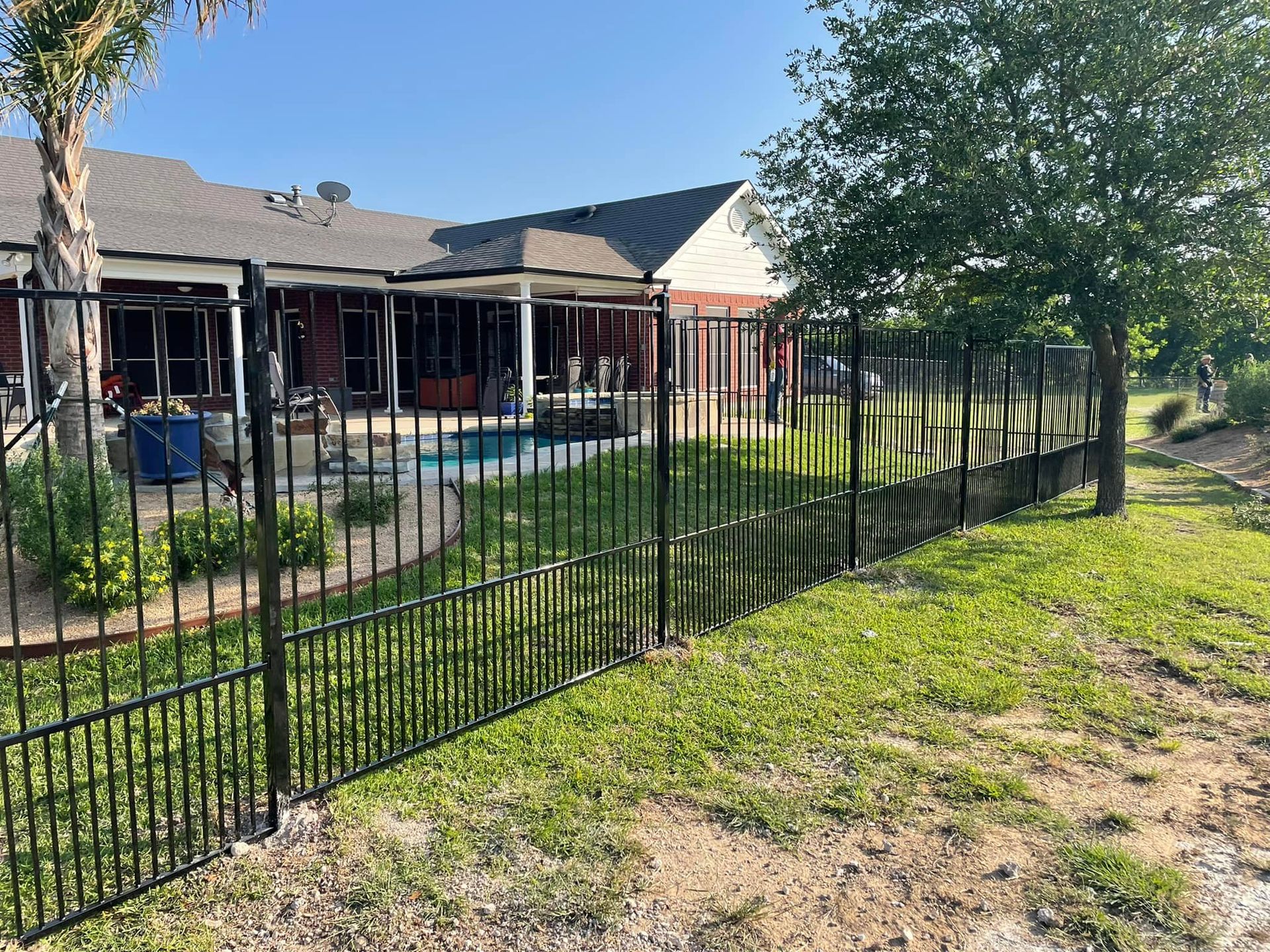 Black metal fence beside a red house and grassy yard on a sunny day