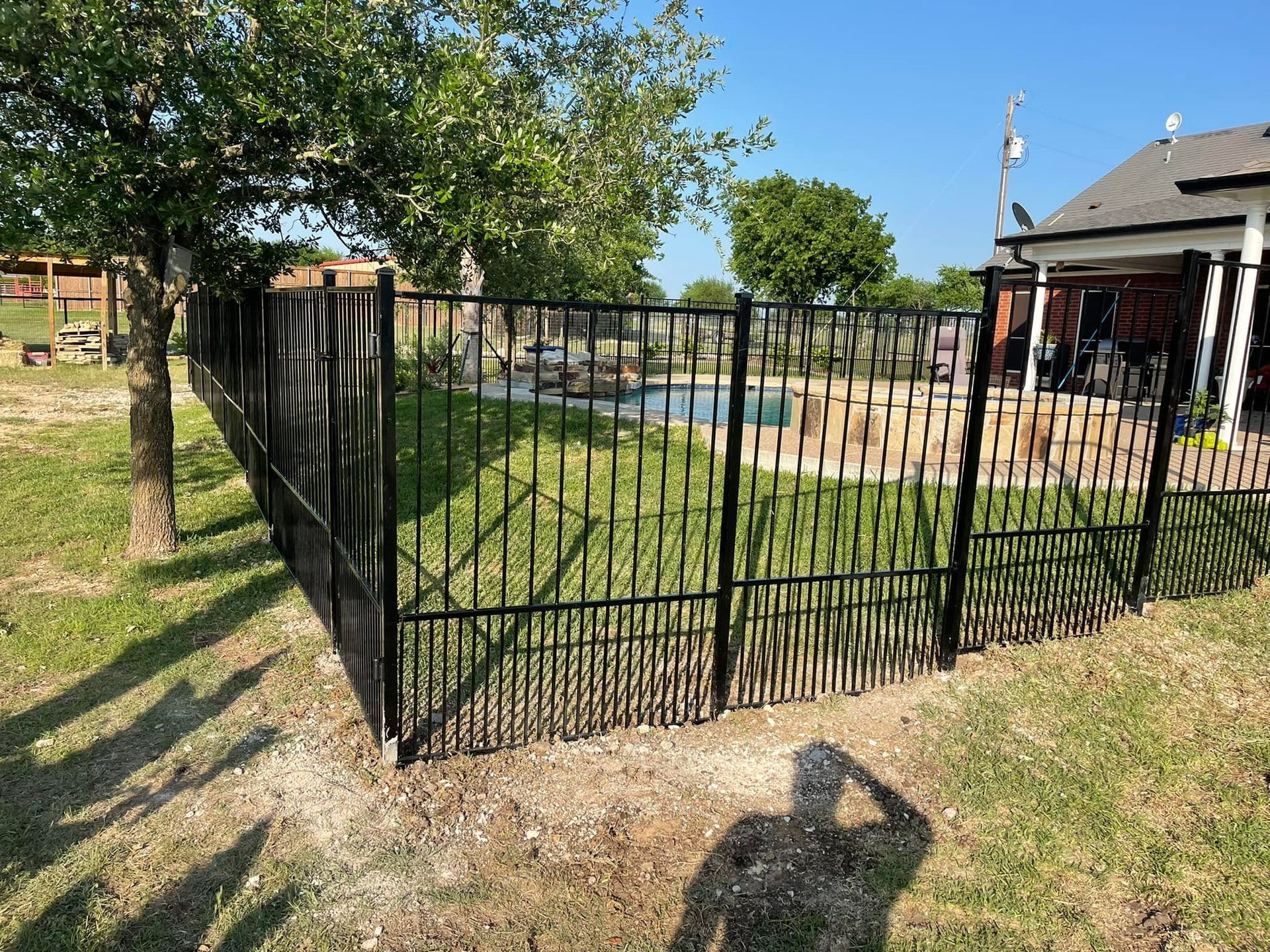 Black metal fence around a yard beside a house and trees on a sunny day