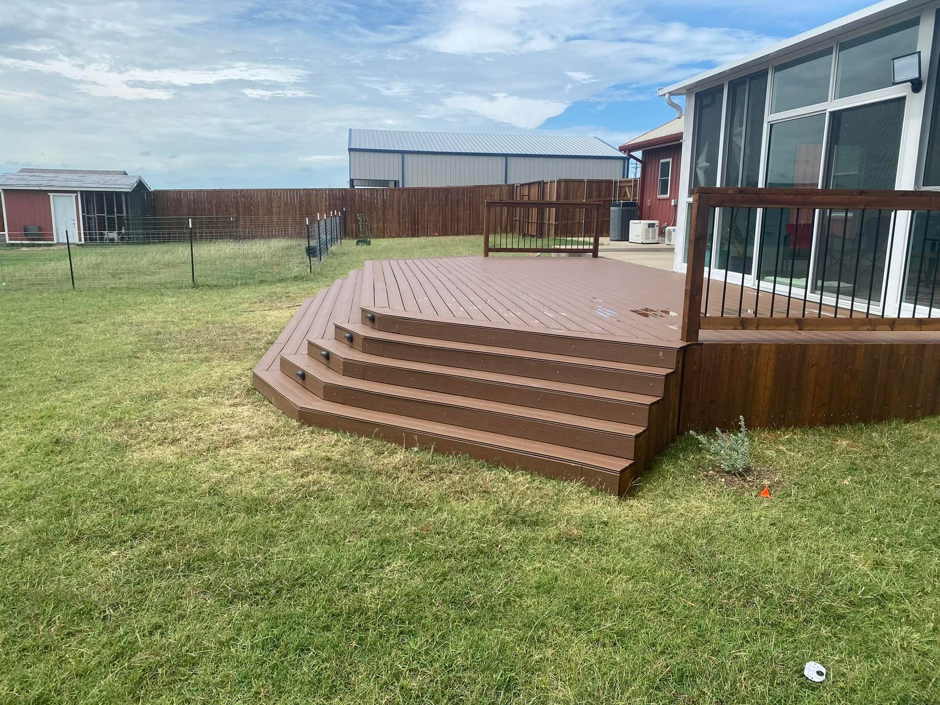 Backyard deck with curved wooden steps beside a grassy yard and modern house windows