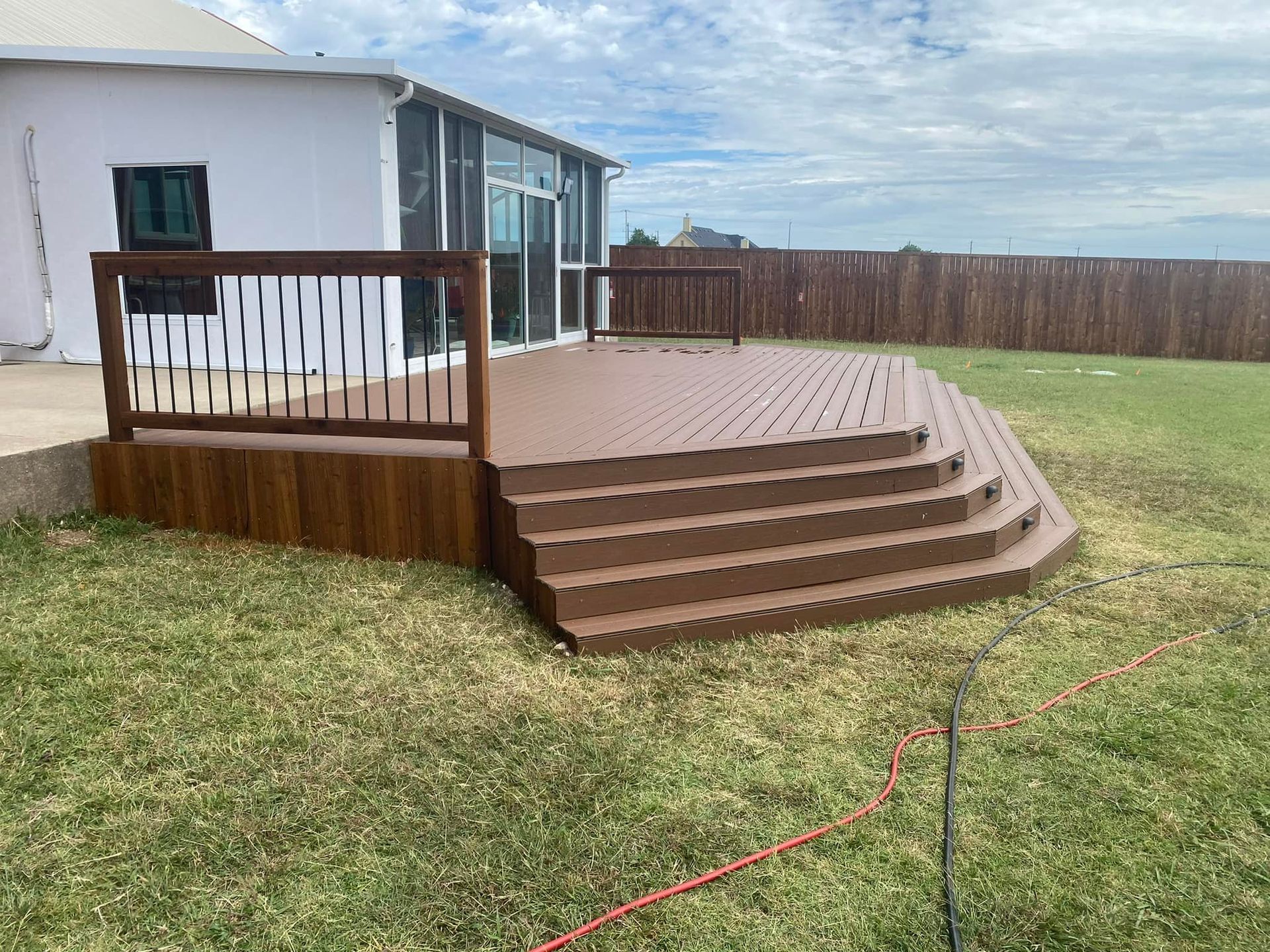 Backyard wooden deck with steps, railing, and a small shed beside a fenced lawn