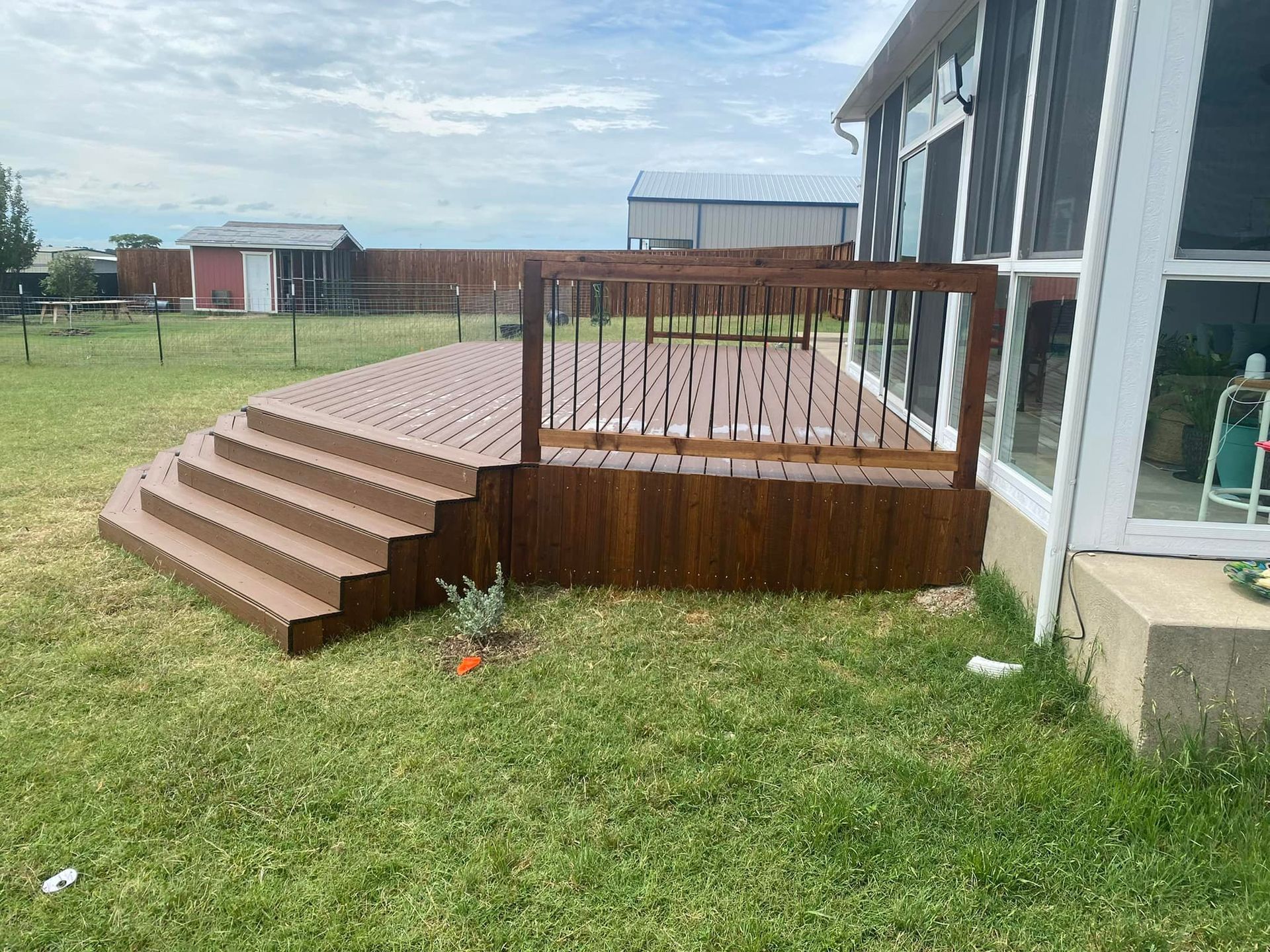 Wooden deck with curved steps and railing beside a house in a grassy yard