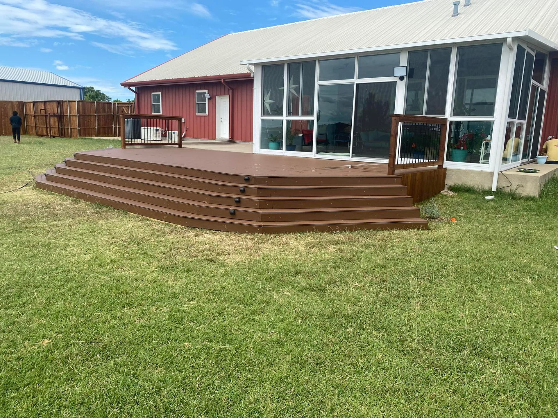 Backyard patio with brown steps, glass sunroom, and green lawn under a cloudy sky