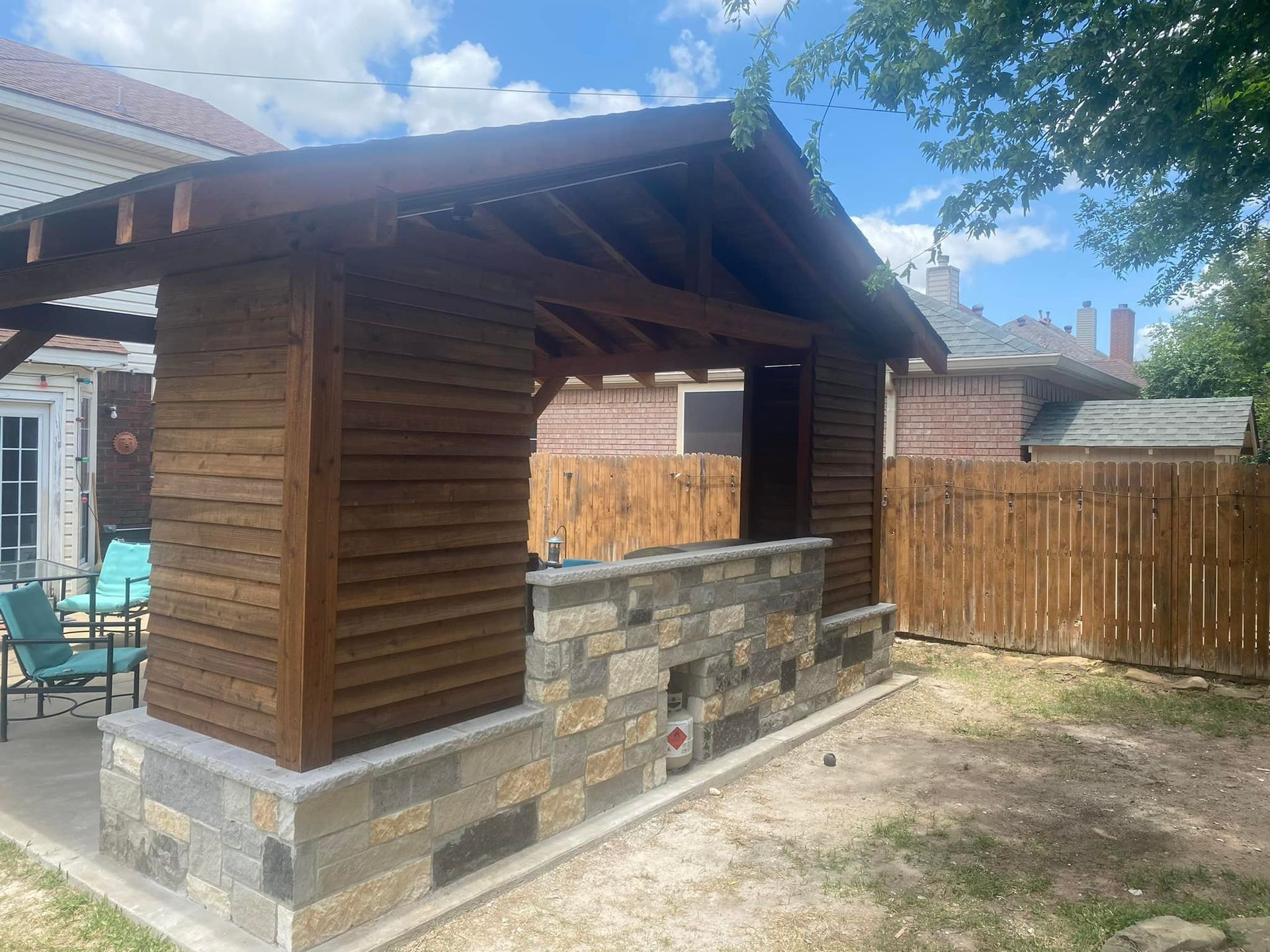 Wooden backyard gazebo with stone bar counter, on a grassy patio under a blue sky