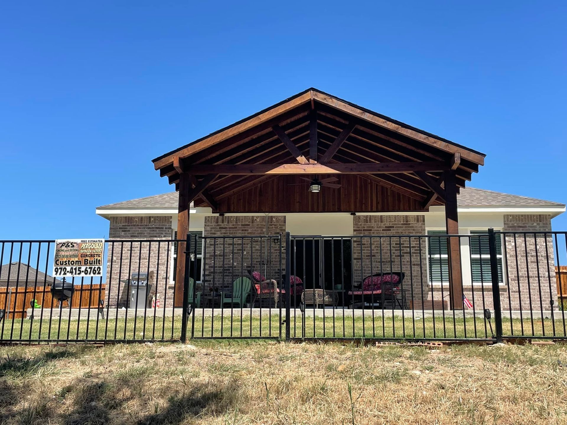 Single-story house with a wooden front porch and black metal fence under a clear blue sky