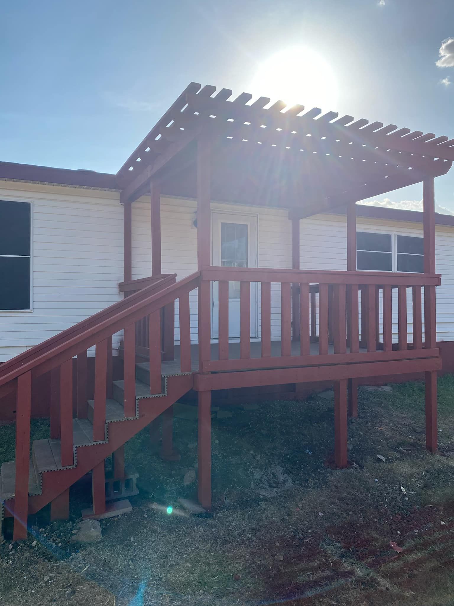 Wooden front porch with stairs and railing on a white house in bright sunlight