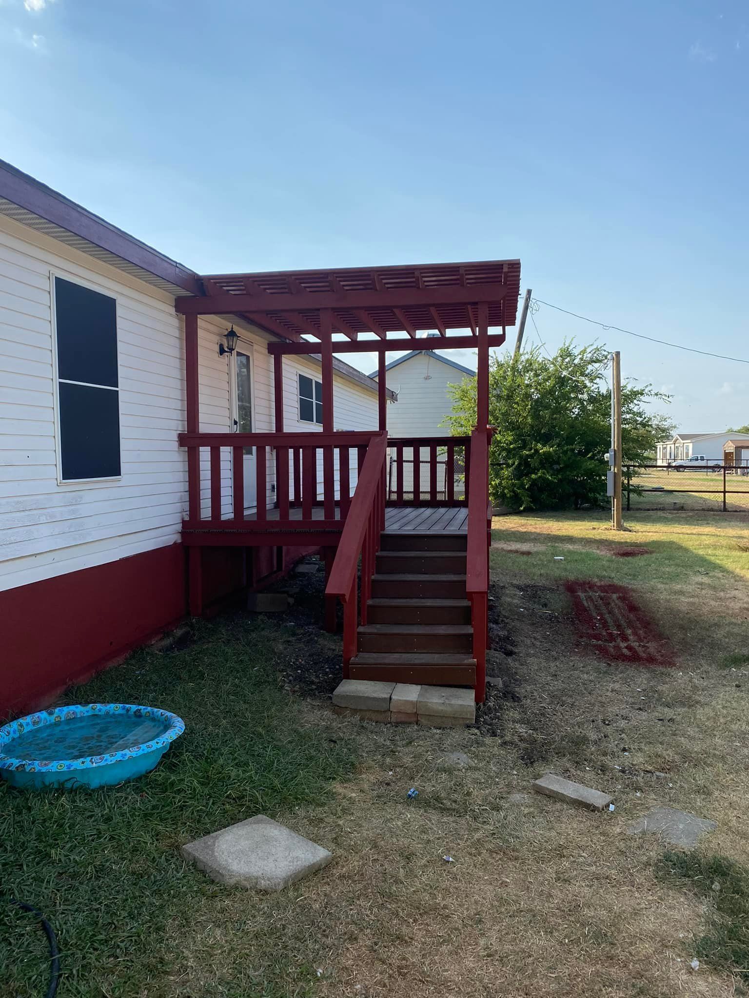 Red wooden porch steps and deck attached to a white house in a grassy yard.