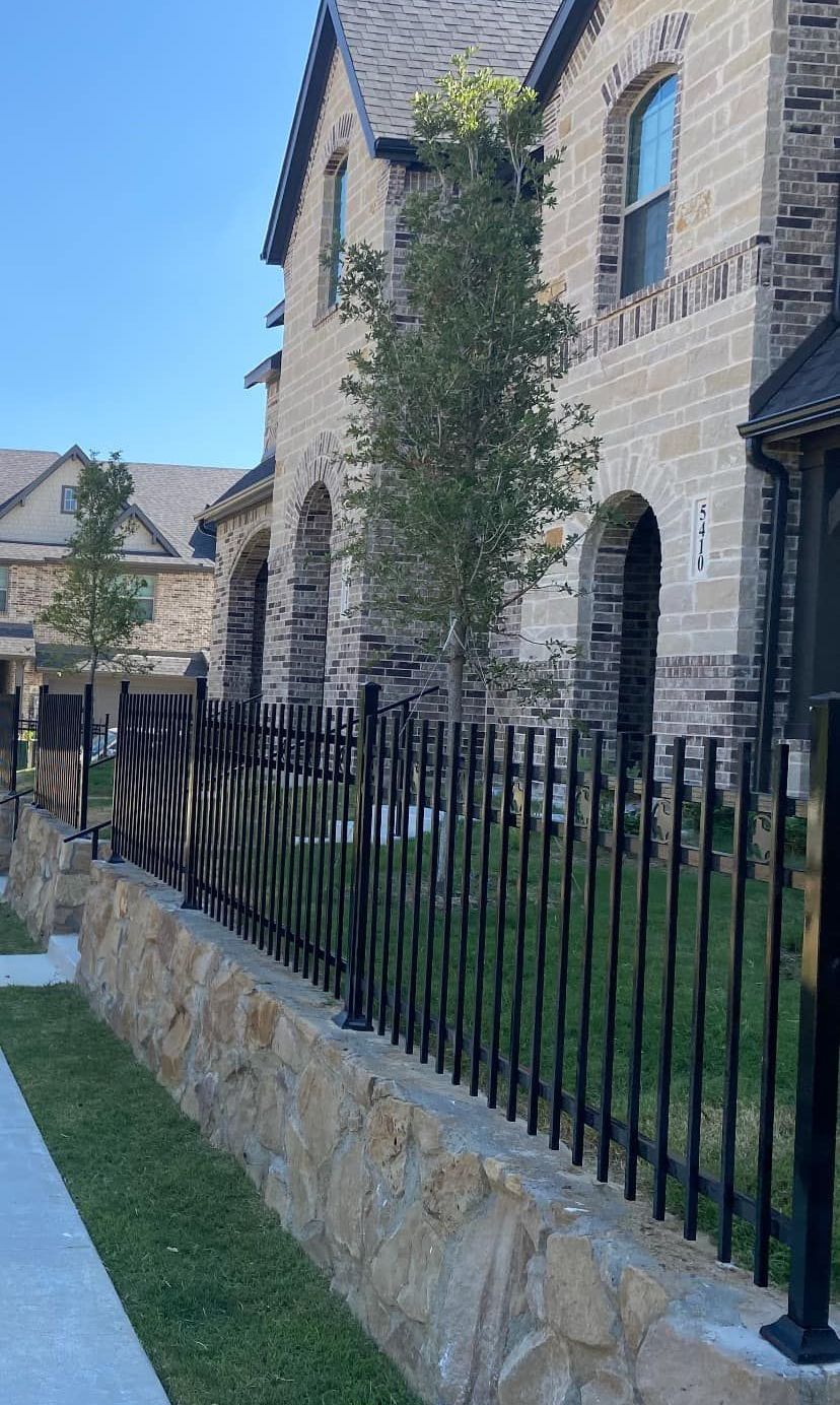 Stone apartment building behind black iron fence and stone wall on a sunny day
