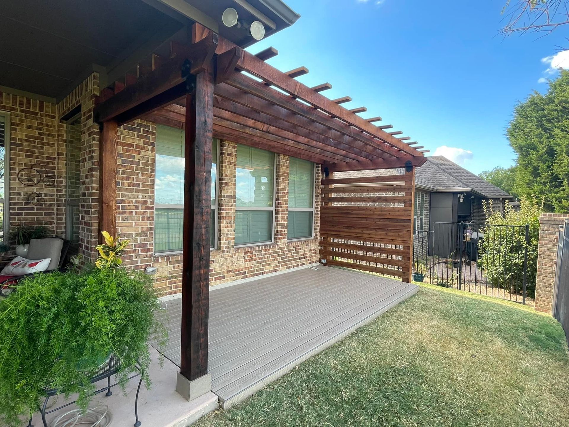 Brick house patio with wooden pergola, paved floor, and small lawn beside a garden shed