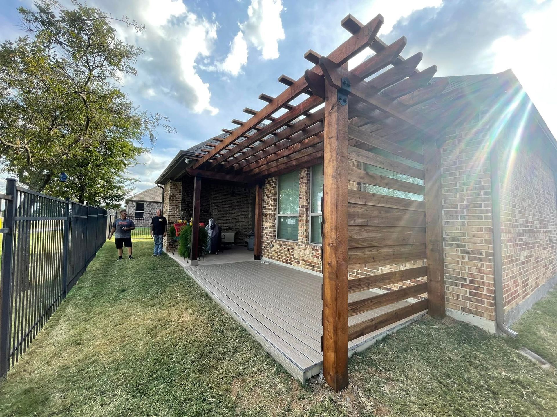 Covered outdoor walkway beside a brick building with a wooden pergola and grassy yard