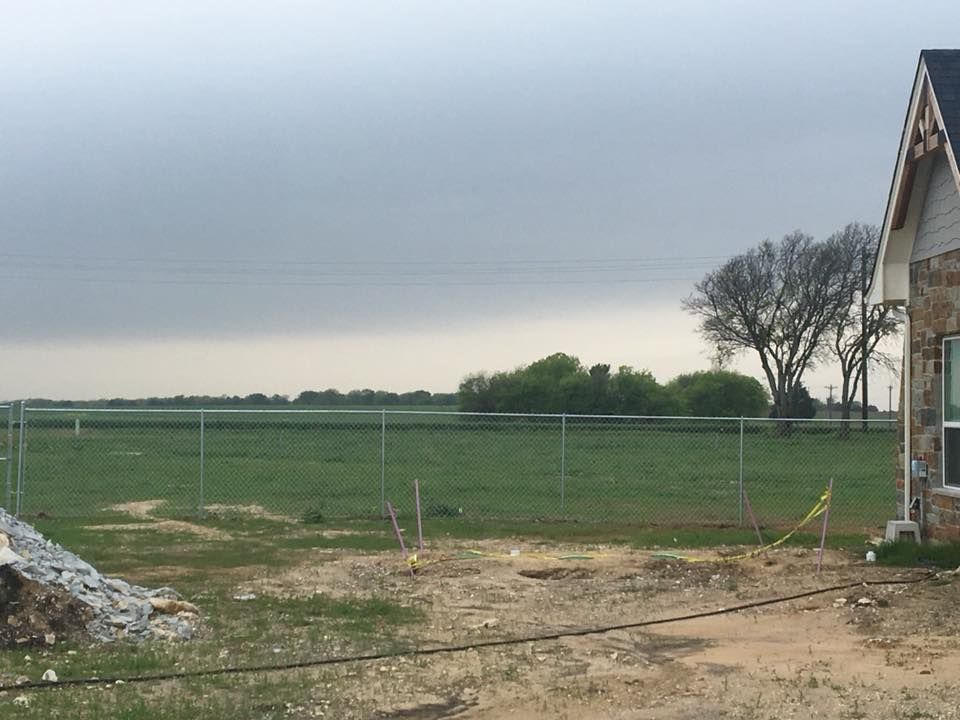 Rural field bordered by a wire fence, with a cloudy sky and a house at the right edge