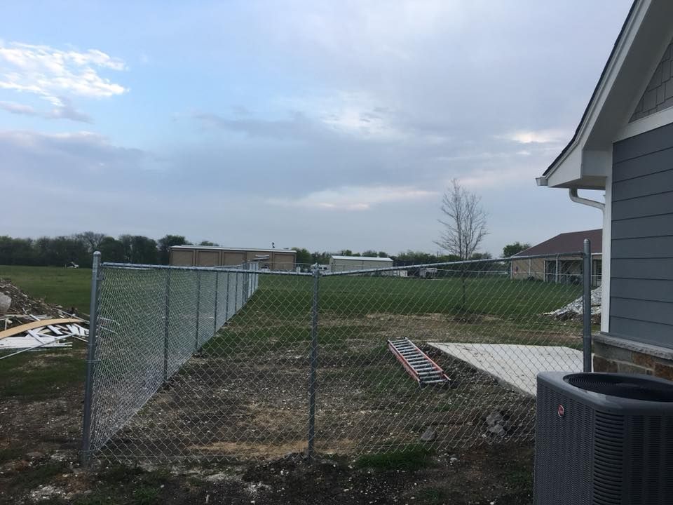 Backyard with chain-link fence, grassy yard, and cloudy sky beside a house