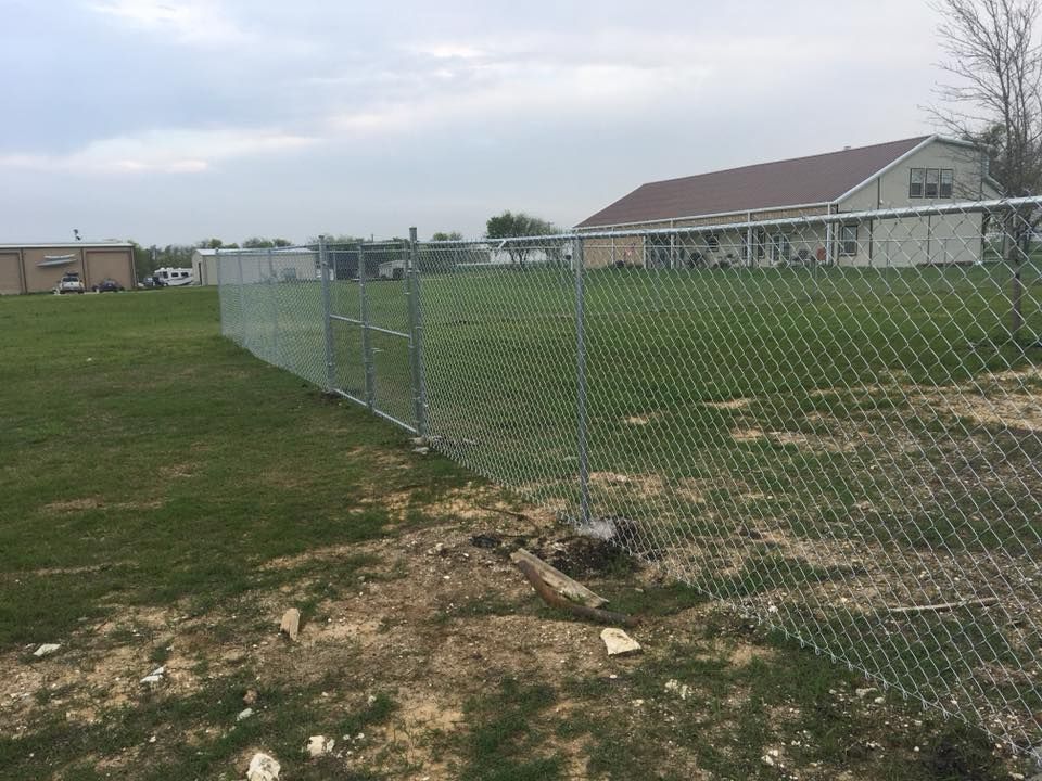 Chain-link fence along a grassy field beside a house under an overcast sky.