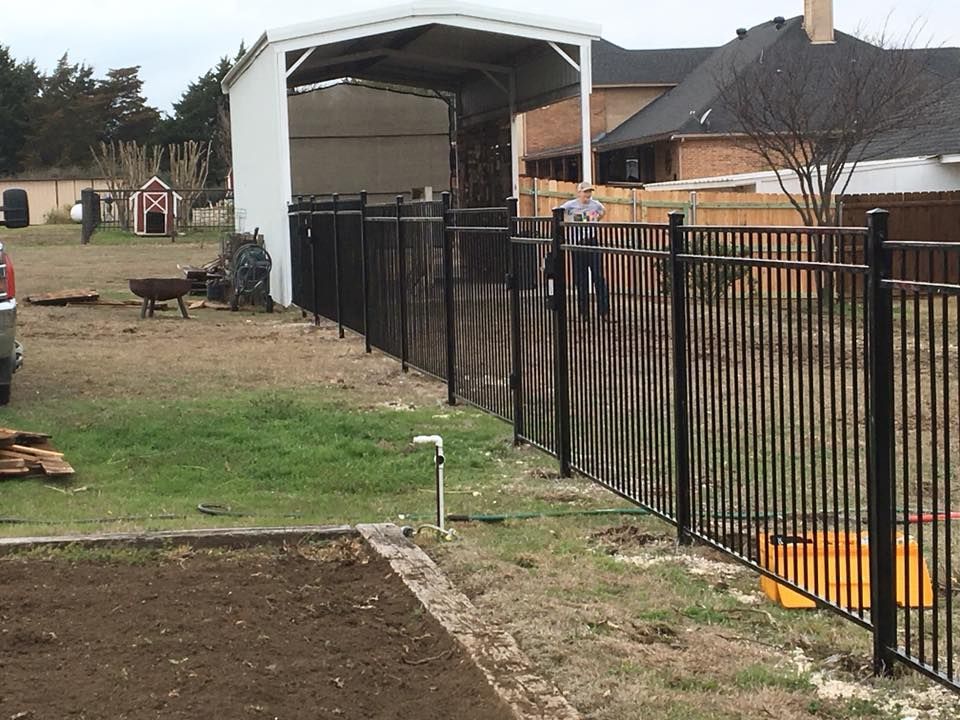 Backyard with black metal fence, covered structure, and bare garden beds on a cloudy day
