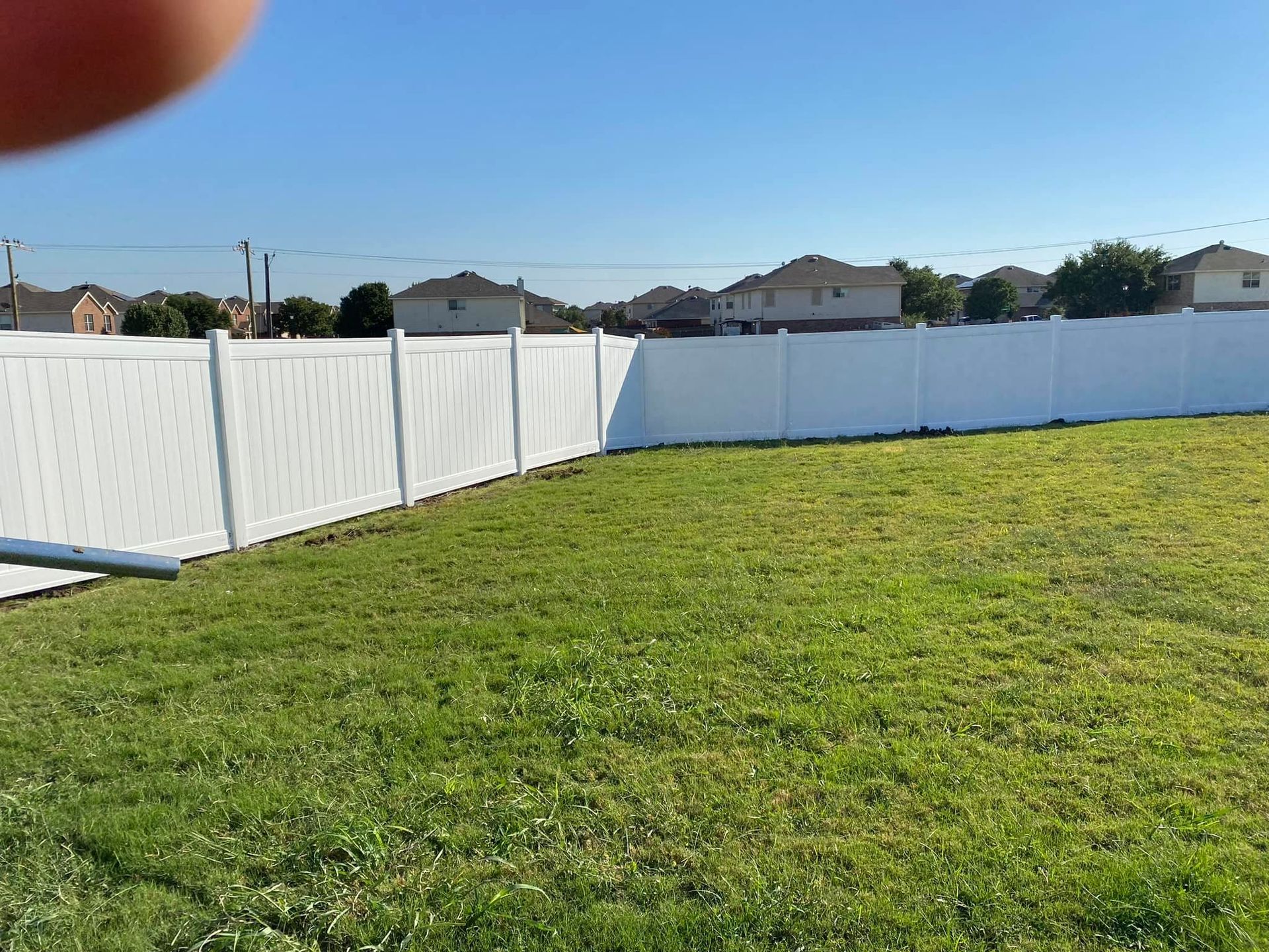 Grassy backyard with a white vinyl privacy fence under a clear blue sky.