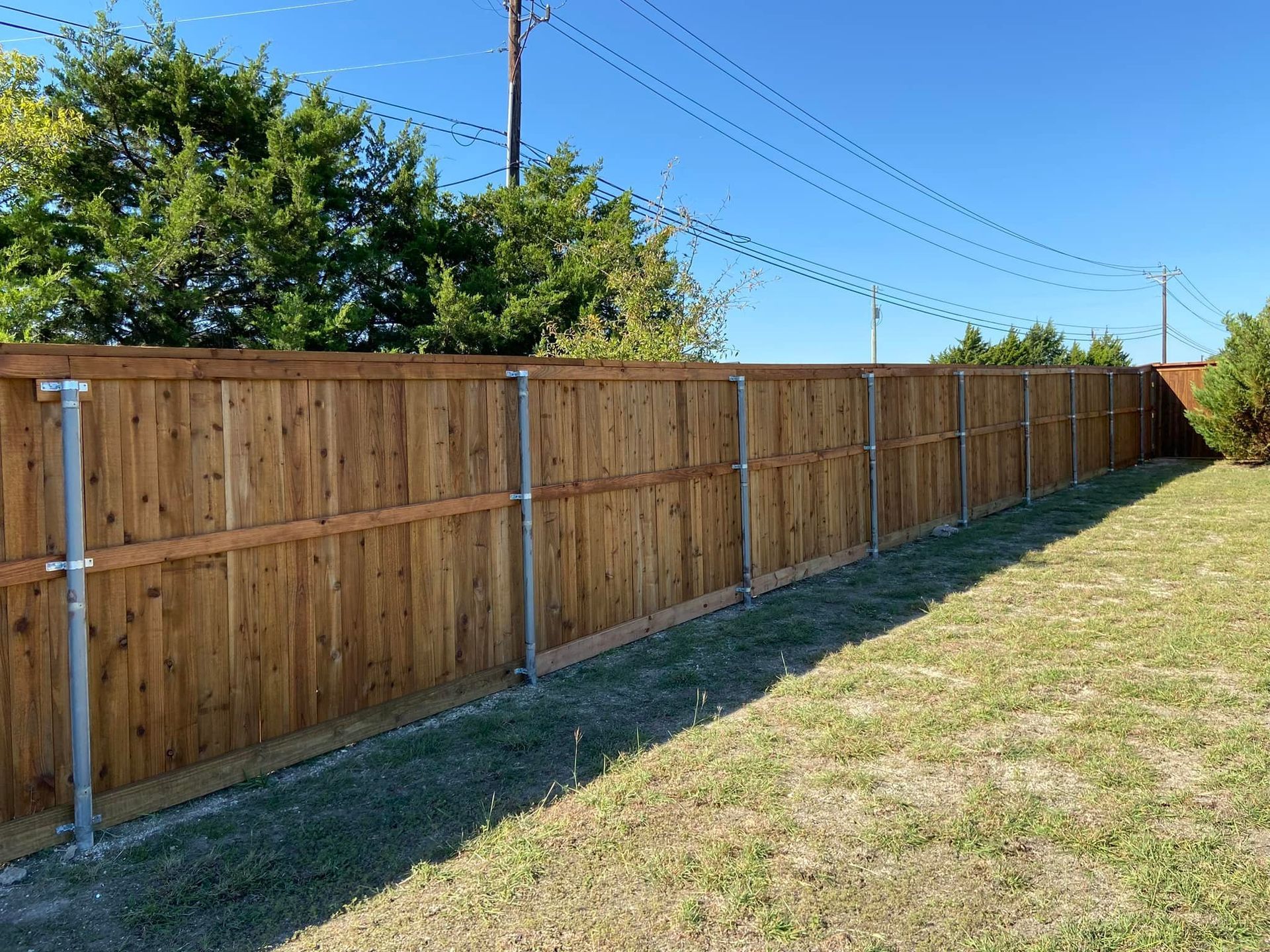 Wooden backyard fence stretching along a grassy yard under a clear blue sky