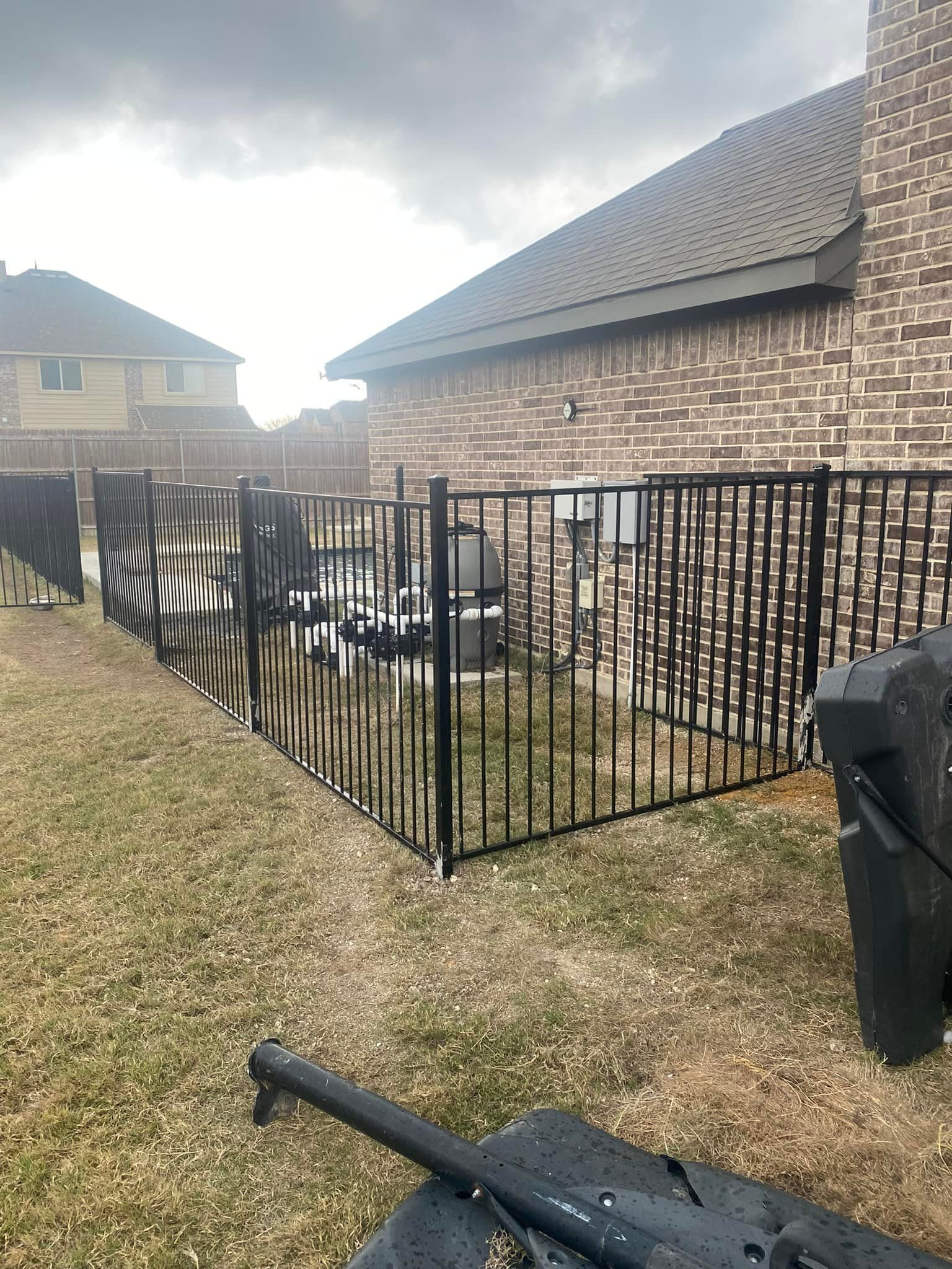 Backyard with black metal fence, brick house, patio furniture, and grill under a cloudy sky