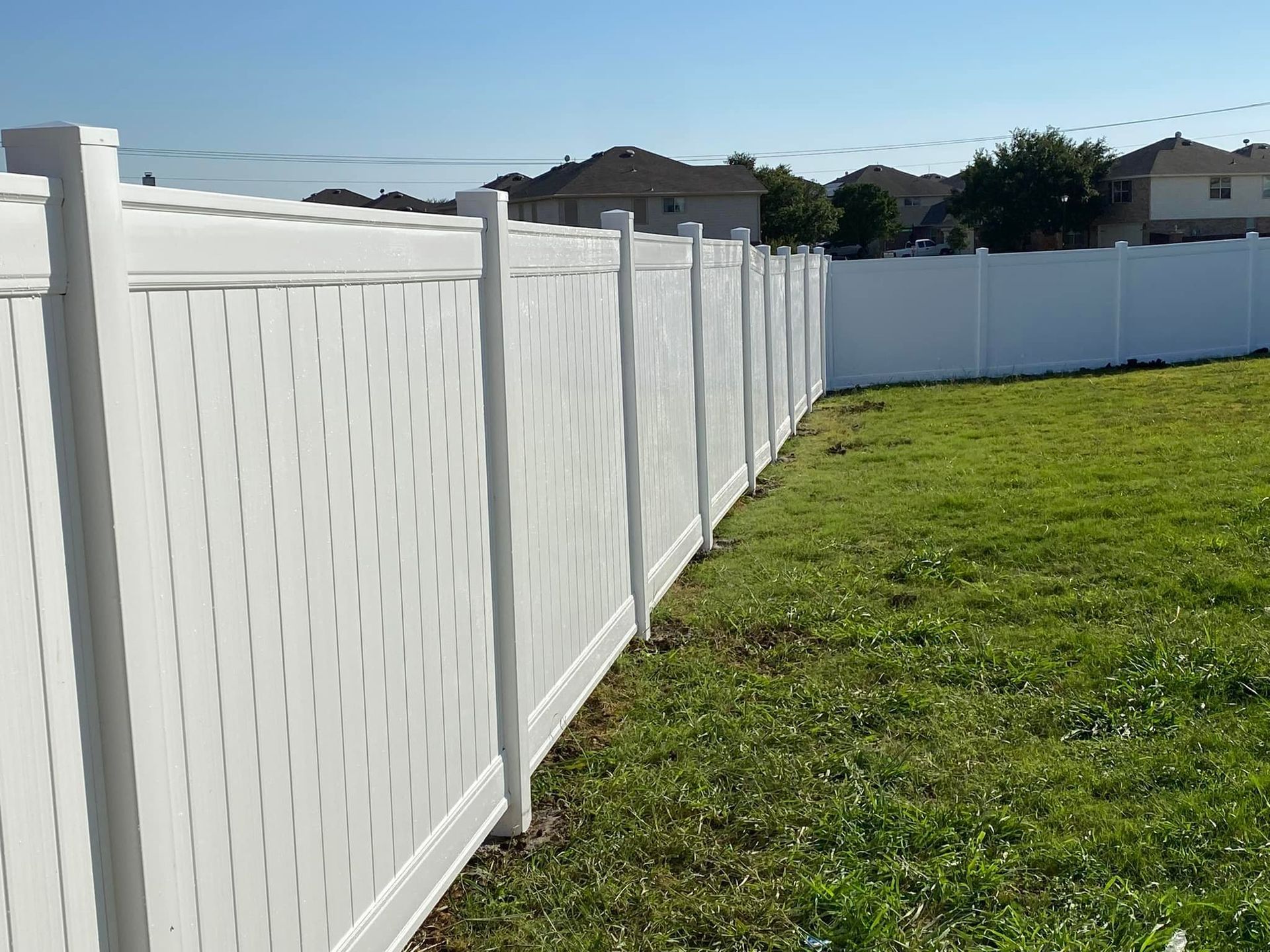 White vinyl fence along a green grassy yard under a clear blue sky.