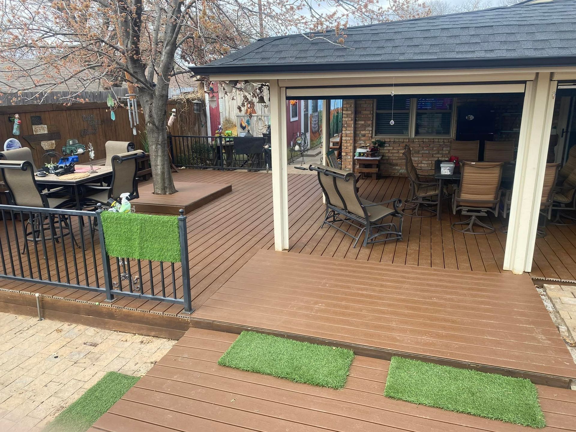 Outdoor patio with tables, chairs, and a covered seating area beside a brick walkway and planter boxes.