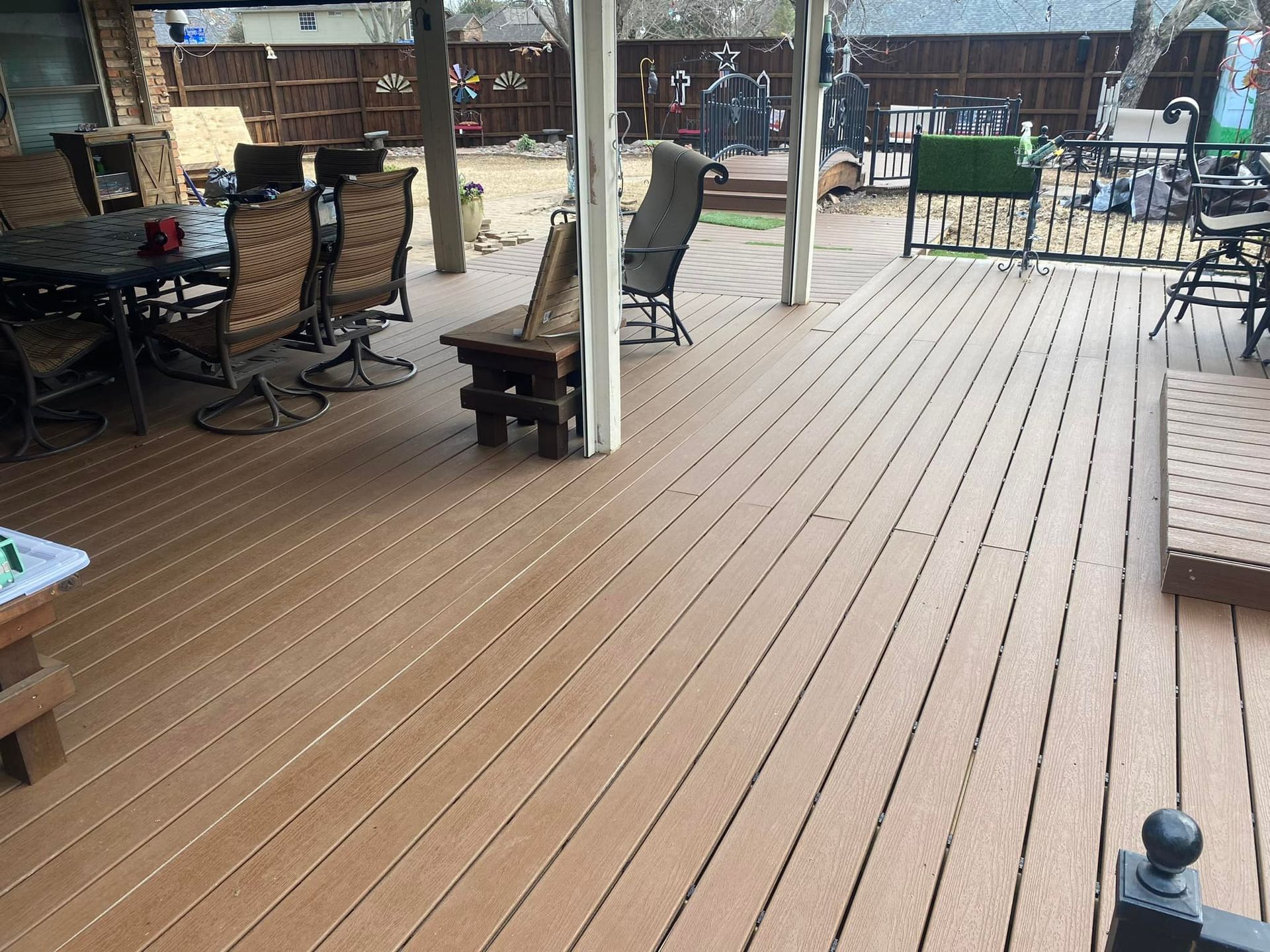 Covered wooden deck with outdoor tables and chairs beside a fenced yard