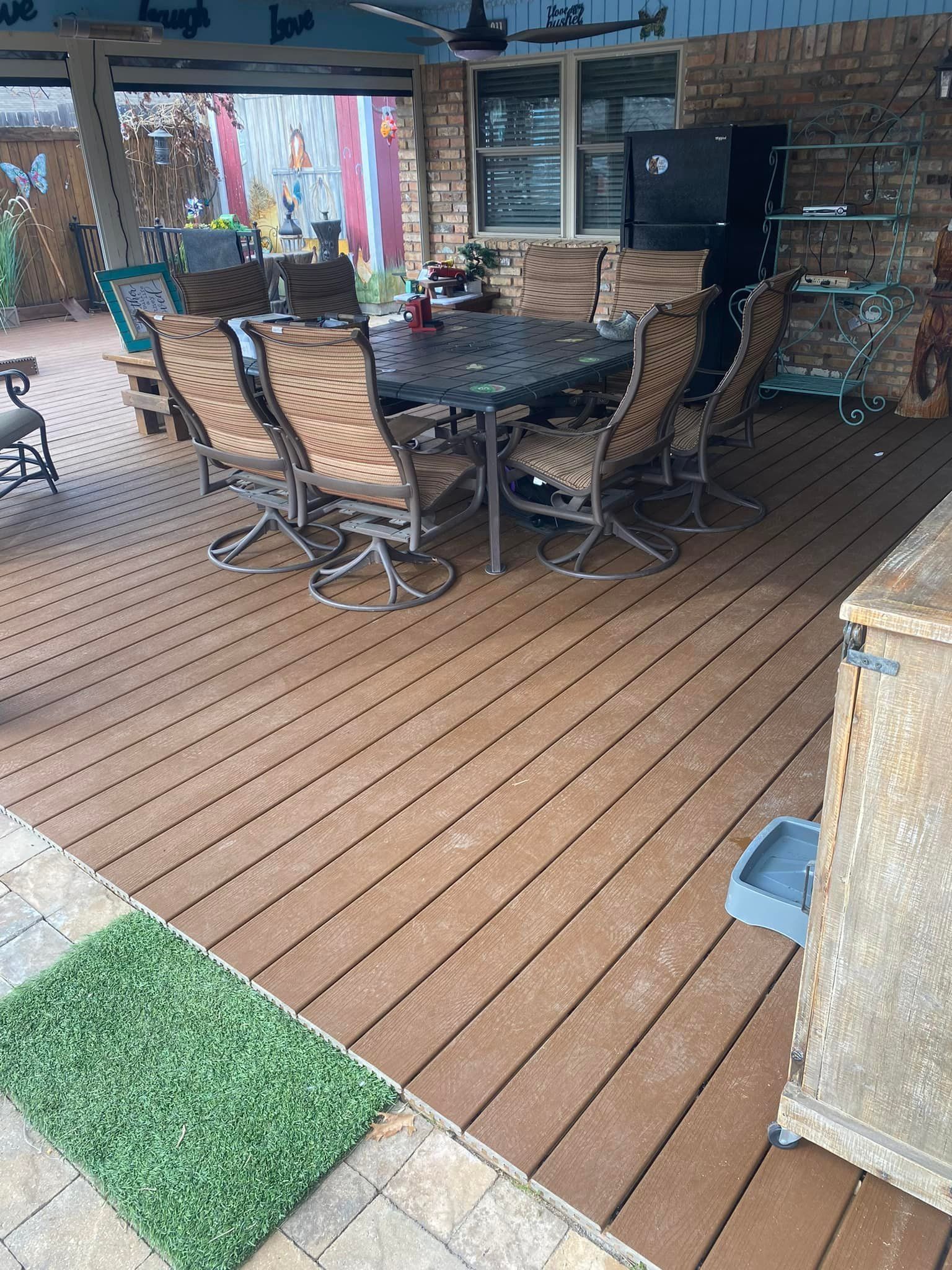 Covered outdoor patio with a large glass dining table and wicker chairs on brown decking.