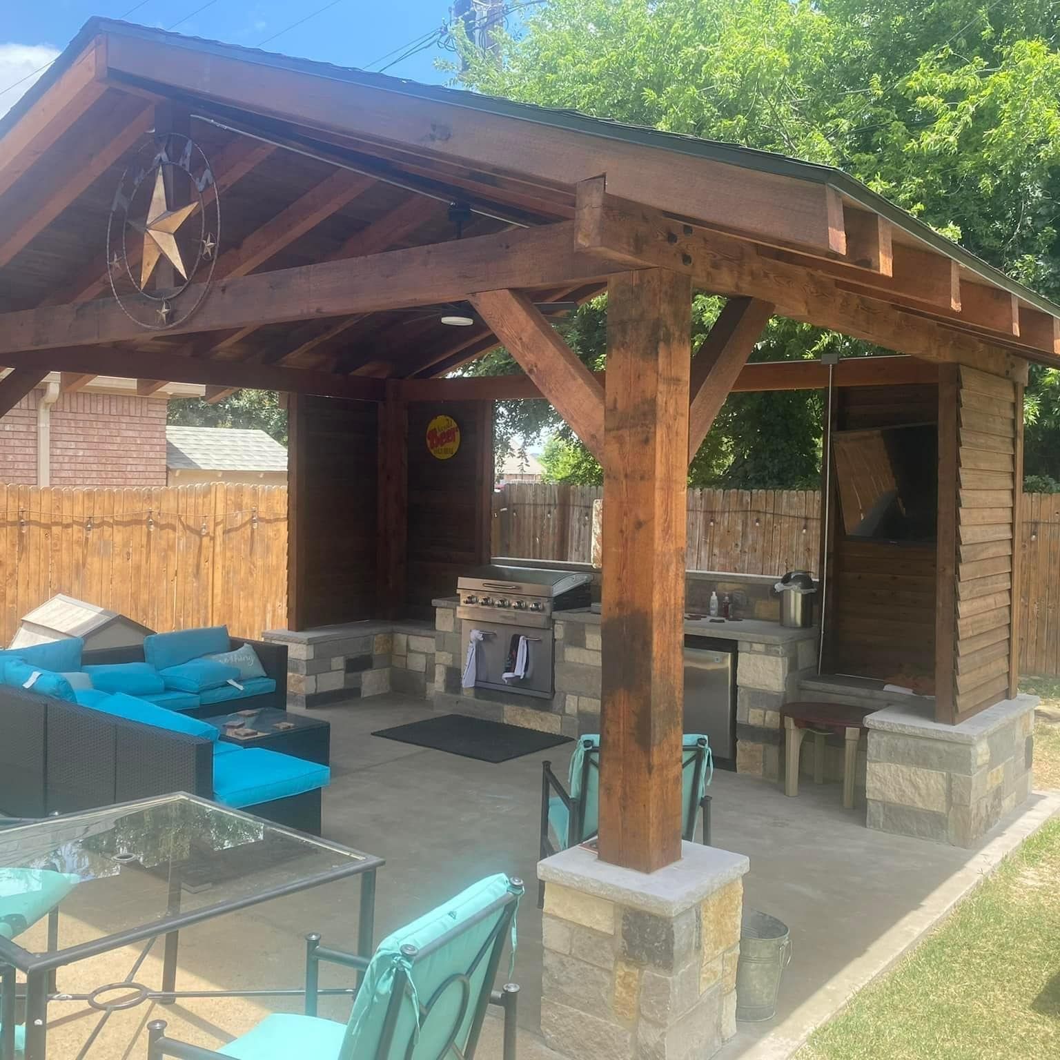 Covered backyard patio with wooden pergola, outdoor seating, and grill area with stone bar stools.