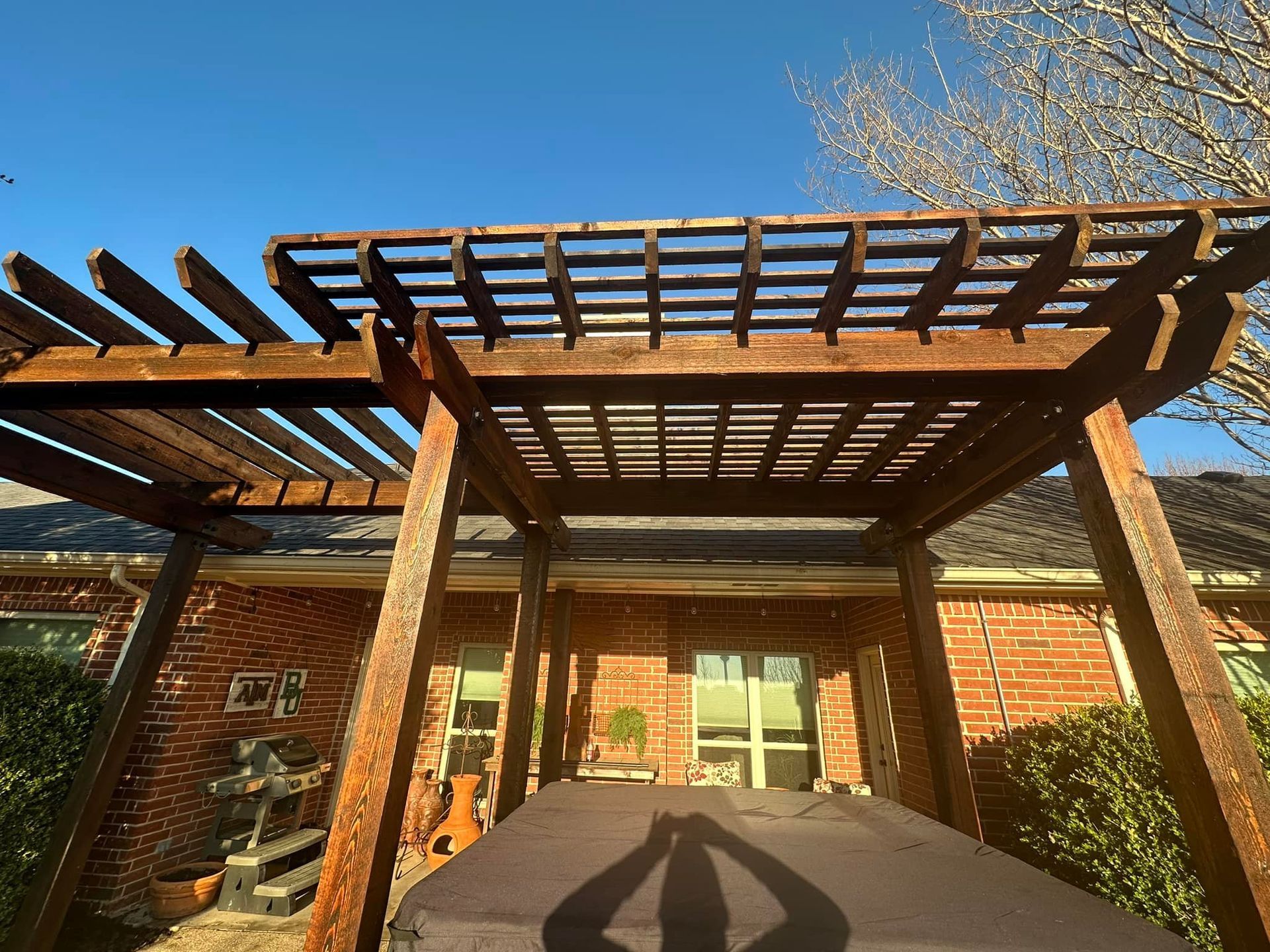 Wooden pergola over a brick patio outside a house, viewed from below in bright daylight