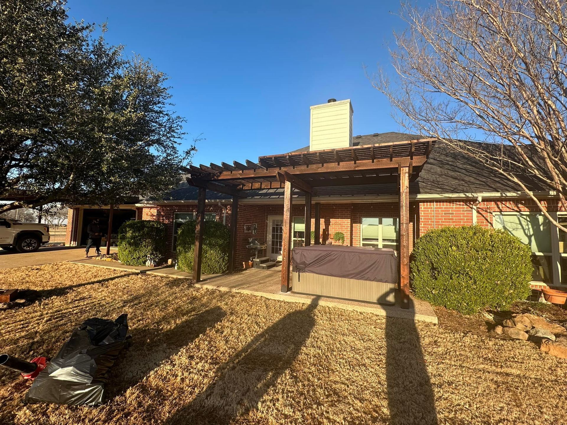 Brick house entrance with covered porch, trees, and long shadows in a sunny yard