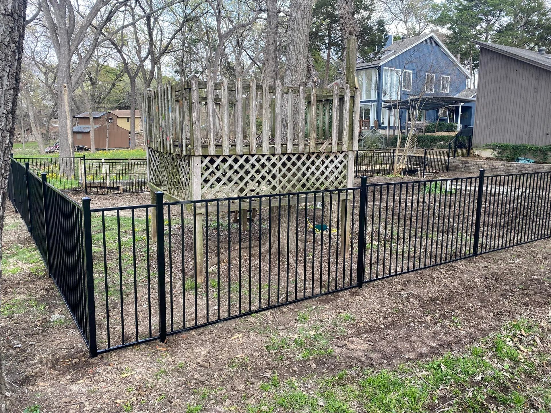 Black metal fence around a yard with trees and a blue house in the background