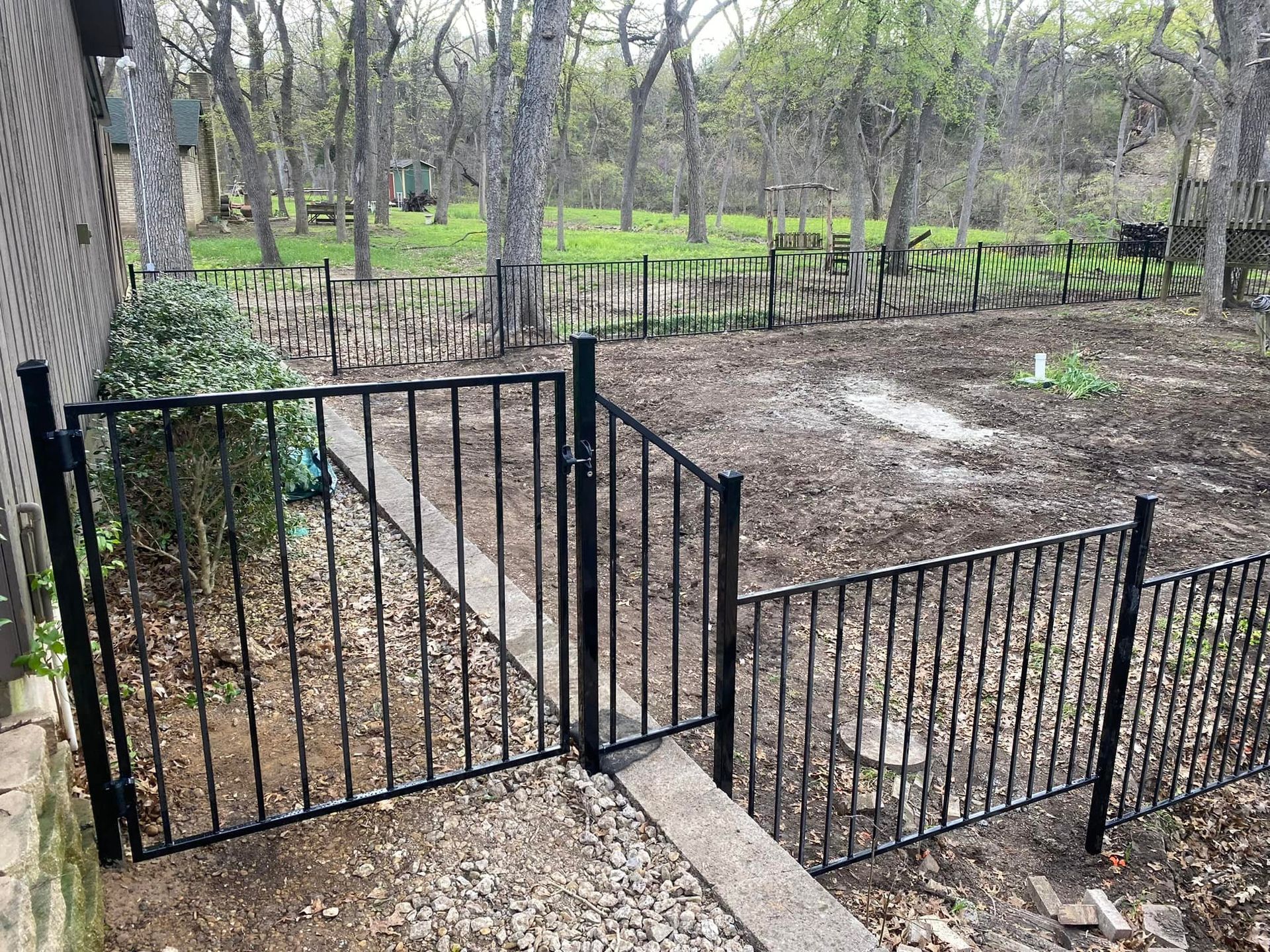 Black metal gate beside a fenced dirt yard in a wooded park area