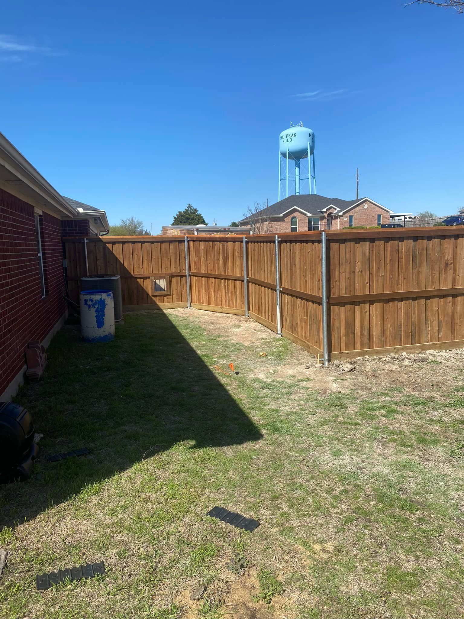 Backyard with wooden fence, grassy yard, and blue water tower under a clear sky.