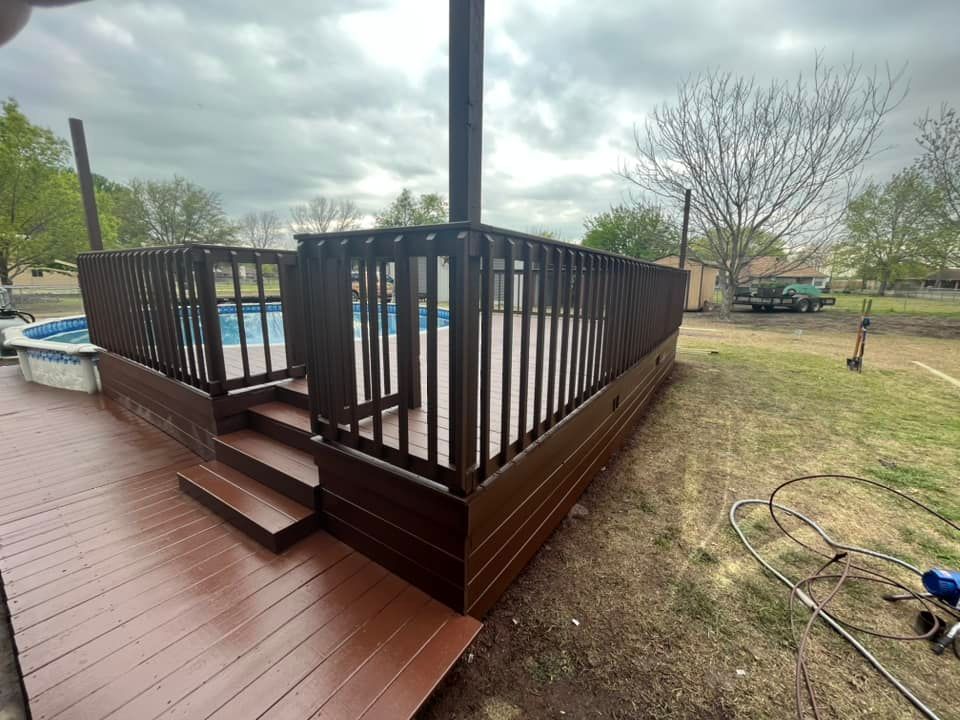 Brown wooden deck with steps and railing in a grassy backyard under cloudy sky