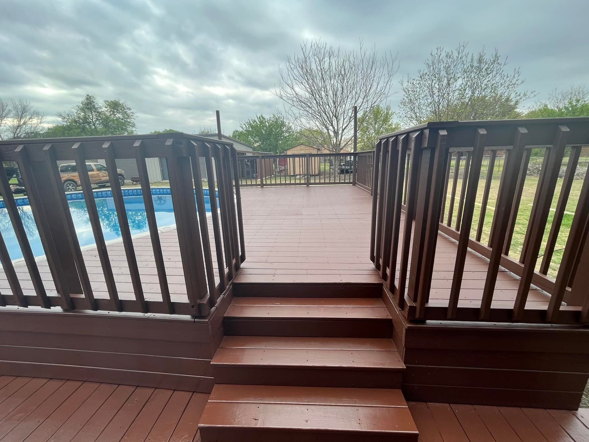 Wooden pool deck with steps and railings, overlooking a swimming pool and trees