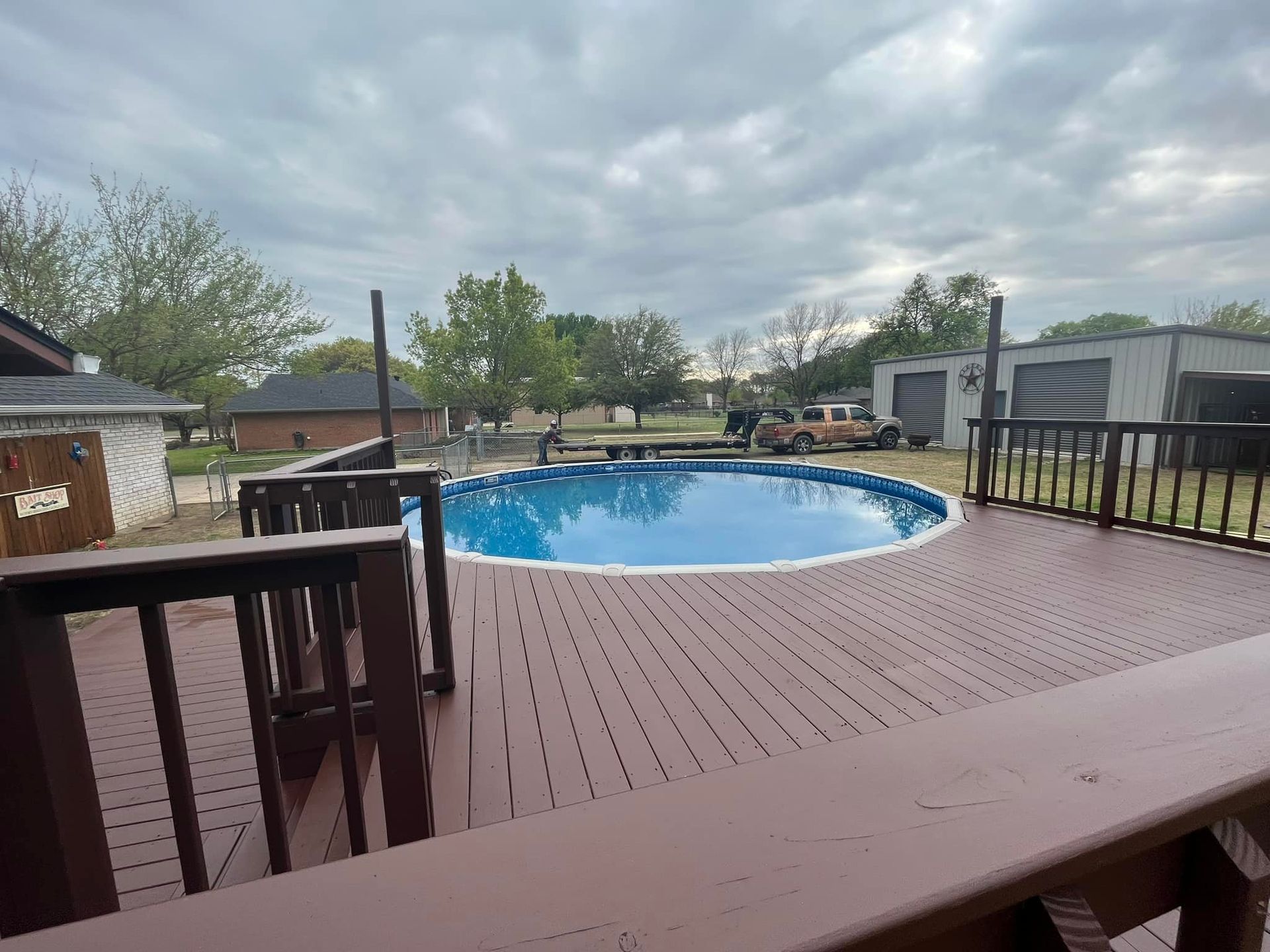 Backyard deck with a round blue pool and wooden railing under a cloudy sky