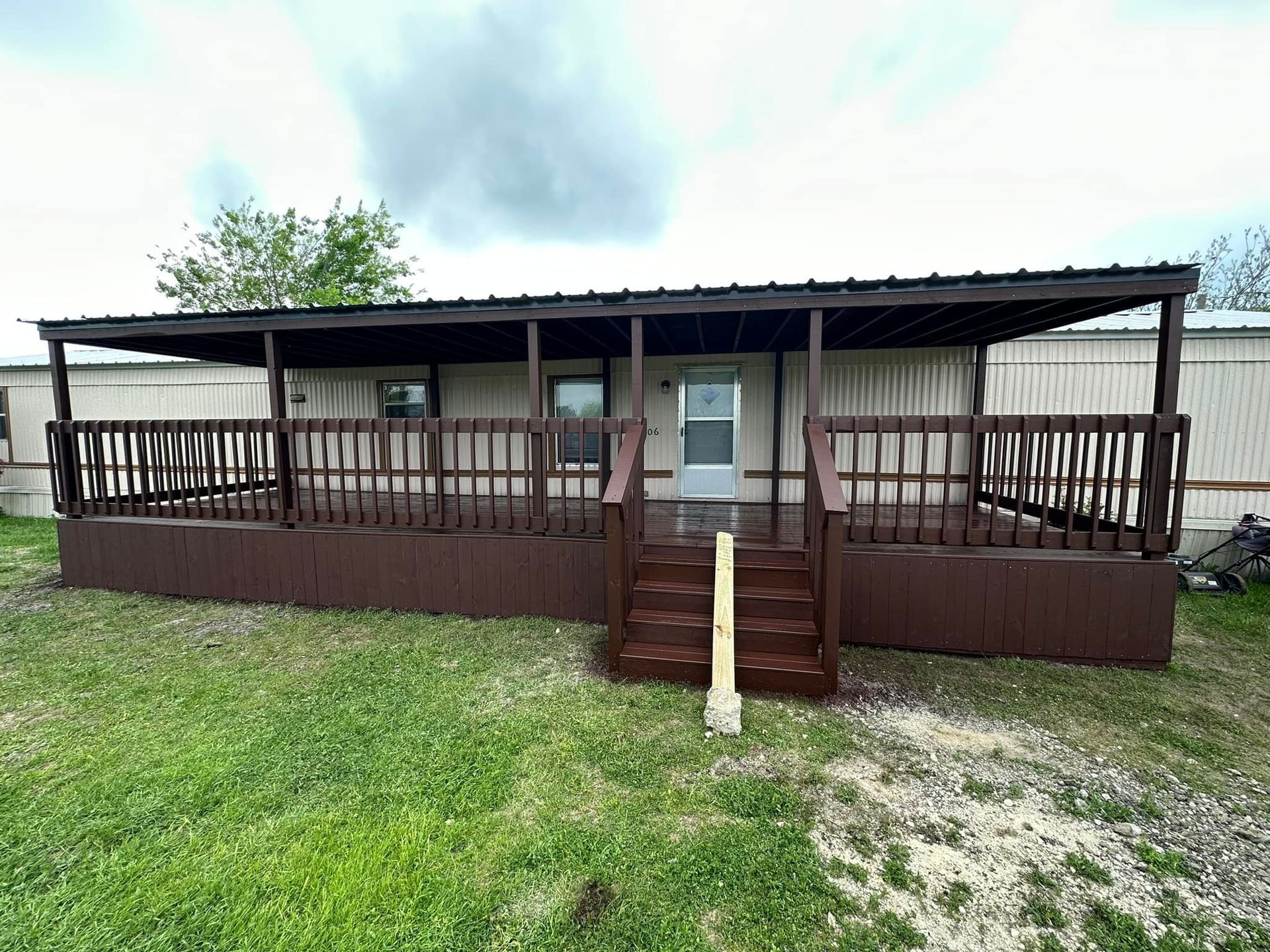 Front view of a brown wooden porch with steps and railing on a grassy yard under a cloudy sky