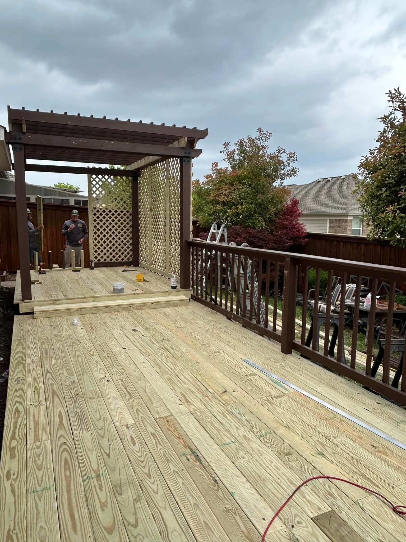 Outdoor wooden deck walkway with a pergola, railing, and cloudy mountain view