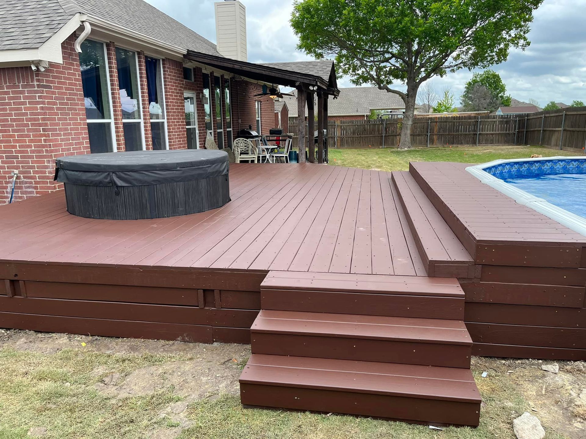 Backyard deck with steps, hot tub, and swimming pool beside a brick house