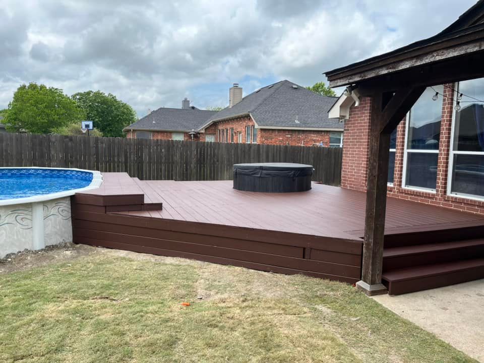 Backyard deck with hot tub, pool edge, wooden fence, and cloudy sky