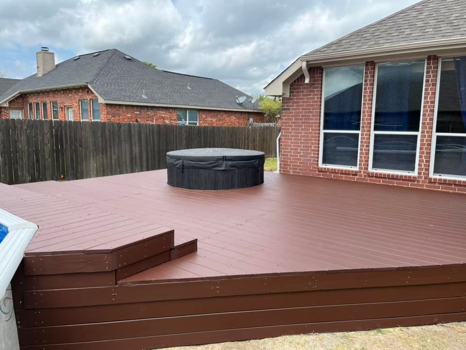 Backyard deck with a circular hot tub, brown steps, and a brick house under cloudy skies