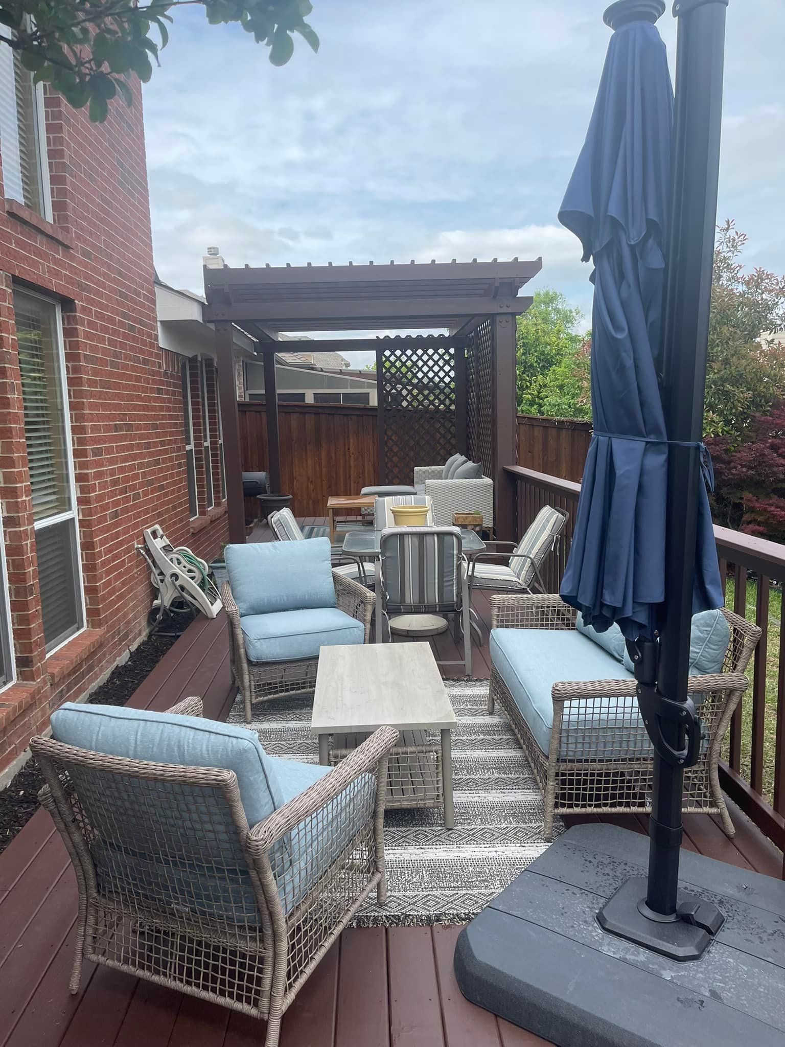 Patio with wicker chairs, blue cushions, tables, and a closed navy umbrella beside a brick wall