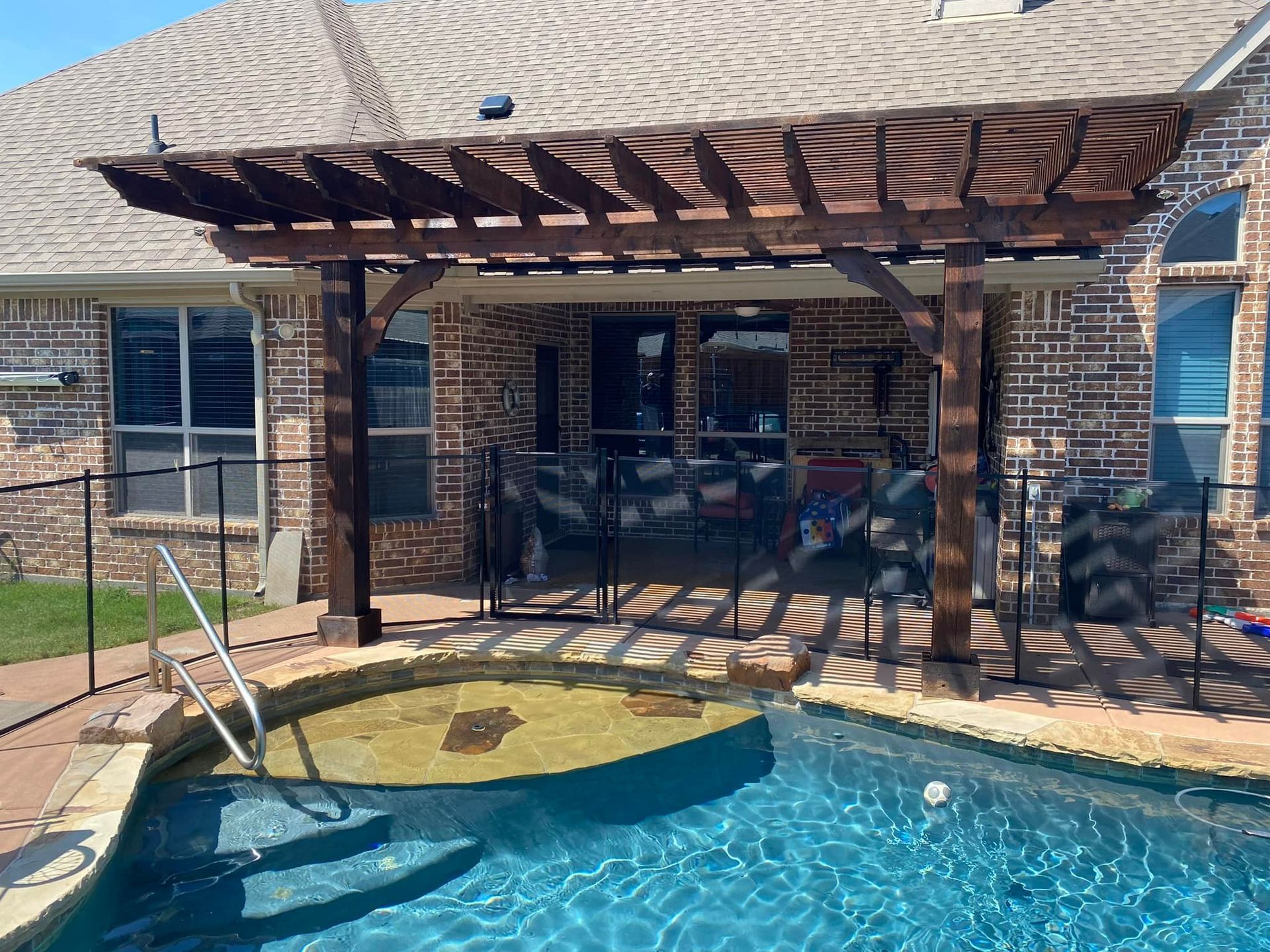 Backyard pool with brick patio, pergola, and lounge chair beside blue water.