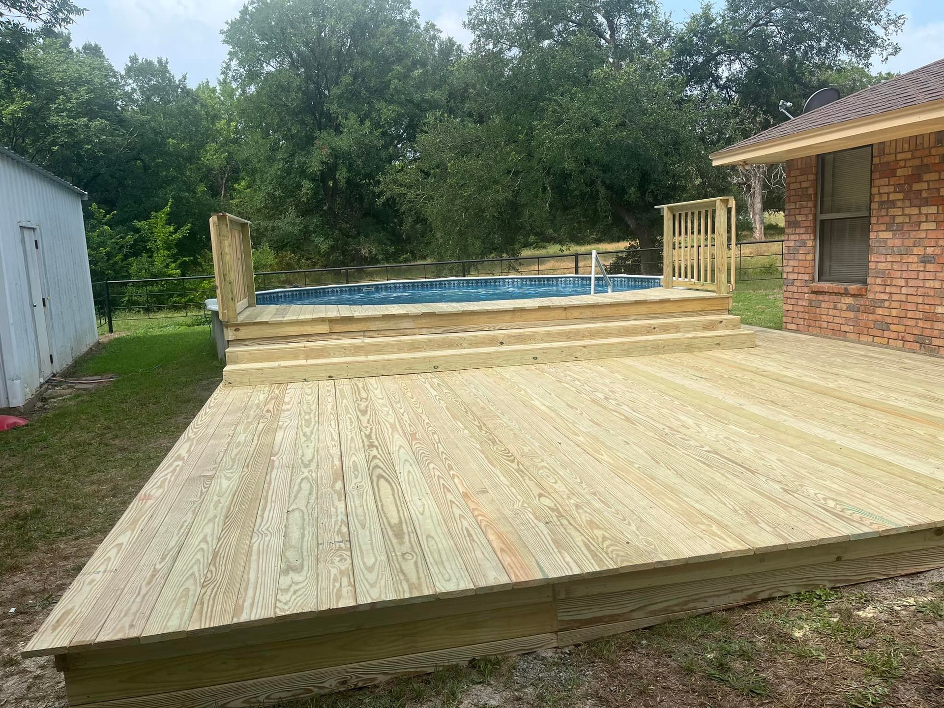 Wooden backyard deck under construction beside a house, with a pool in the background.