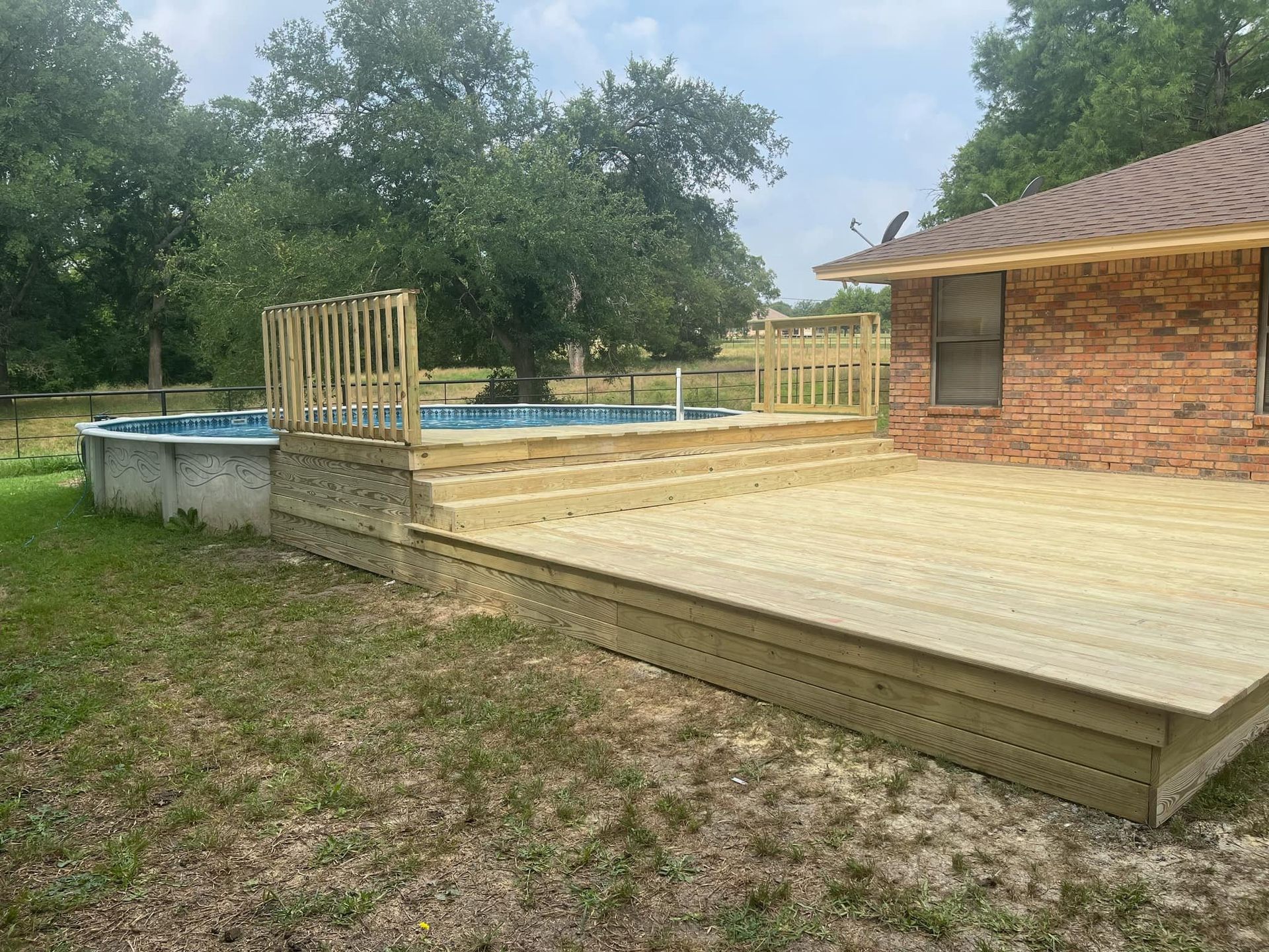 Backyard wooden deck with a hot tub, railing, and brick house beside a grassy yard