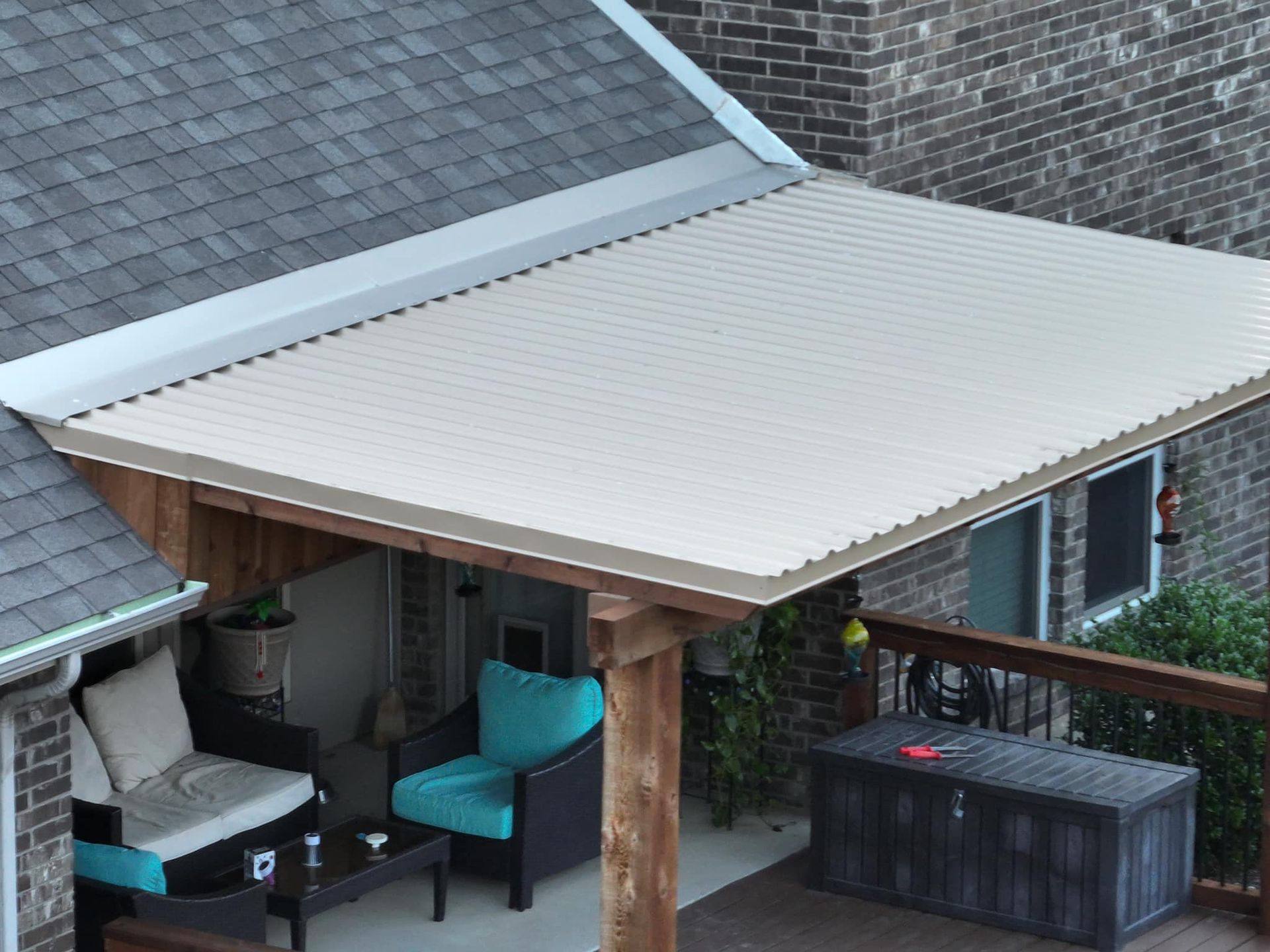 Patio with beige awning, teal chair, and black storage box beside a house roof