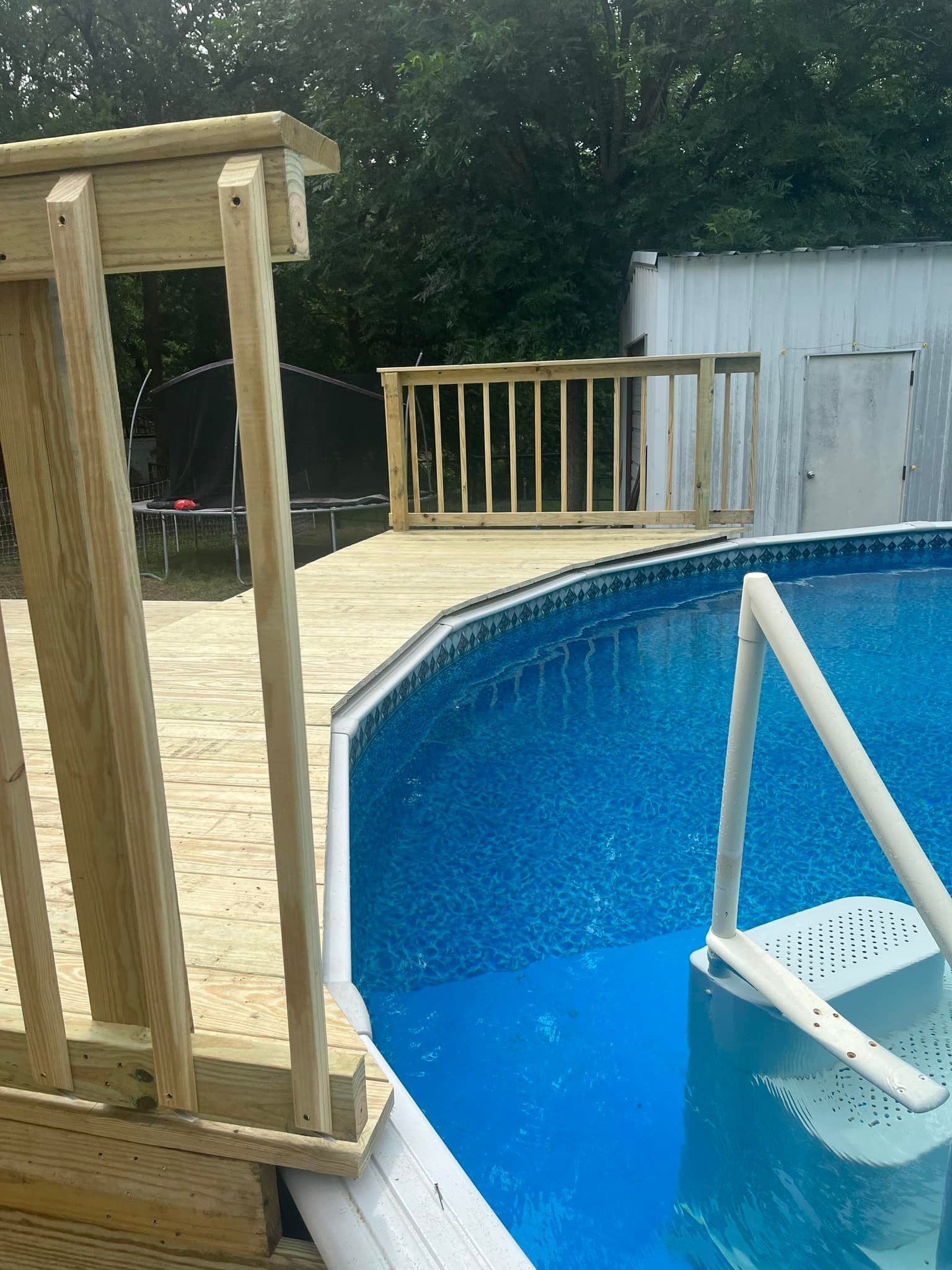 Backyard above-ground pool with a white ladder and wooden deck railing alongside it