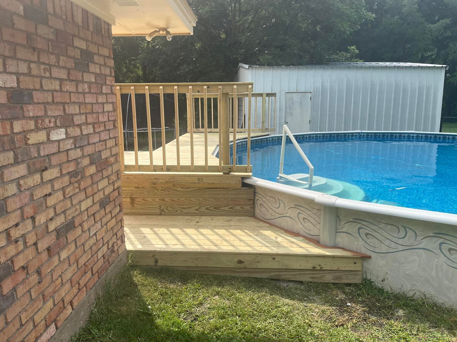 Backyard deck beside a swimming pool with wooden railing, brick wall, and grass lawn
