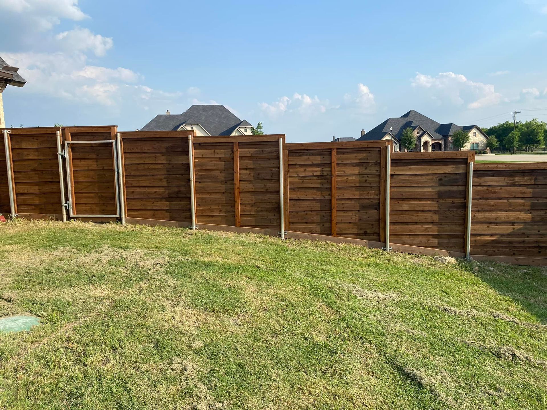 Wooden privacy fence along a grassy yard under a blue sky with houses in the background